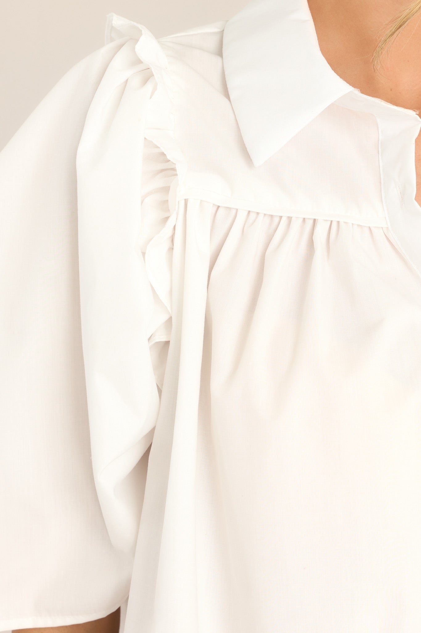 Close up view of this top that features a collared neckline, functional buttons down the front, butterfly short sleeves, and ruffle detailing. 