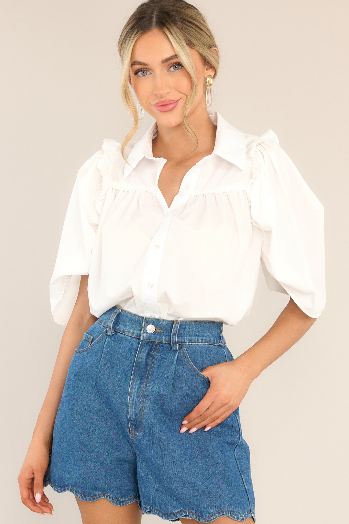 This all white top features a collared neckline, functional buttons down the front, butterfly short sleeves, and ruffle detailing. 