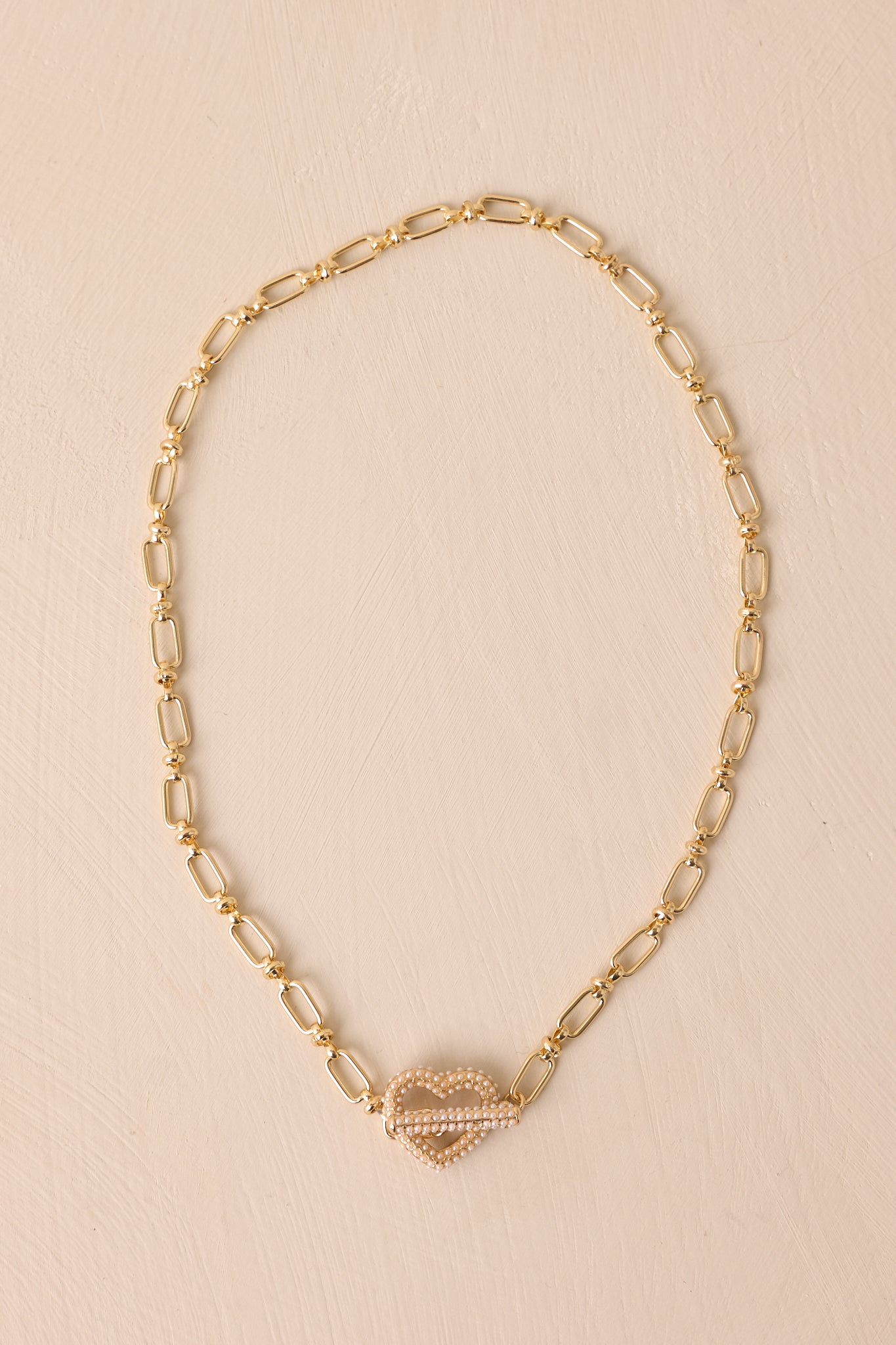 A view of the clasped necklace highlighting the toggle clasp, decorated with small faux ivory pearls, and the delicate gold rectangle chain.