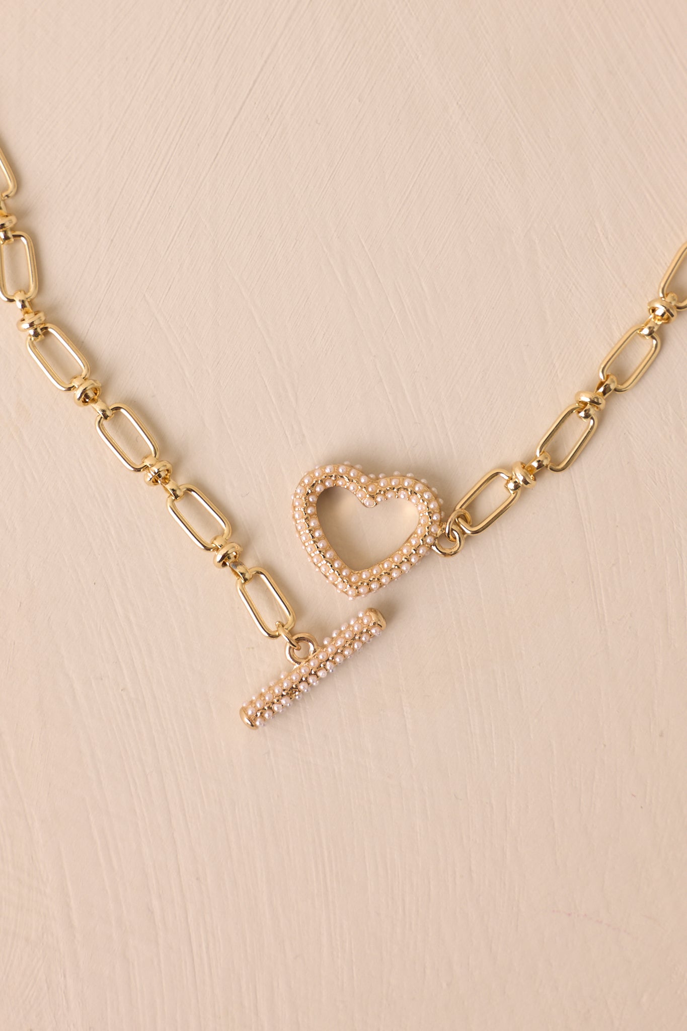 A detailed close-up of the toggle clasp with ivory faux pearls and the gold heart pendant, showcasing the intricate pearl detailing and smooth gold finish.