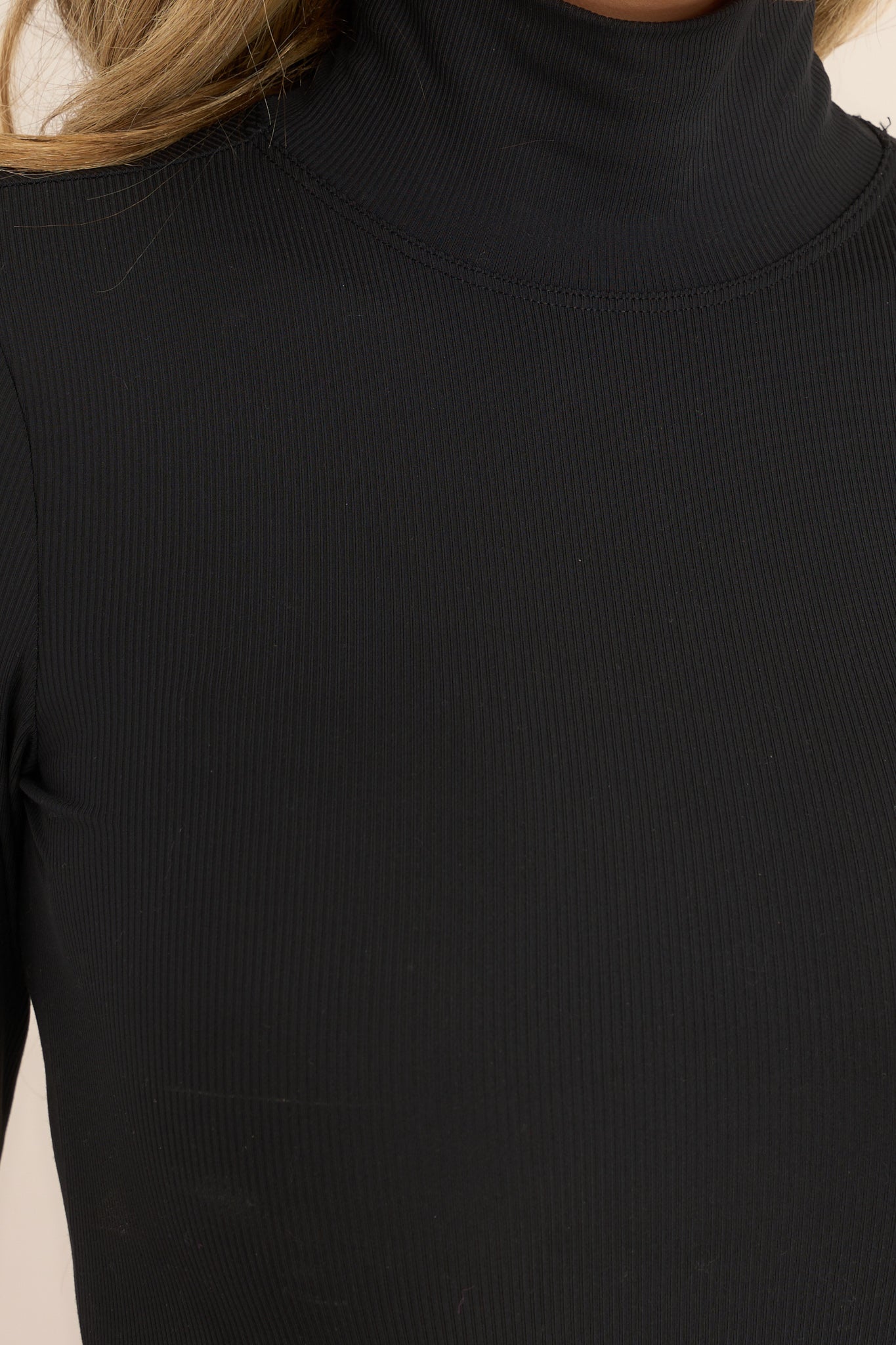 Close up view of this bodysuit that features a turtleneck design, long sleeves, and a ribbed texture throughout.