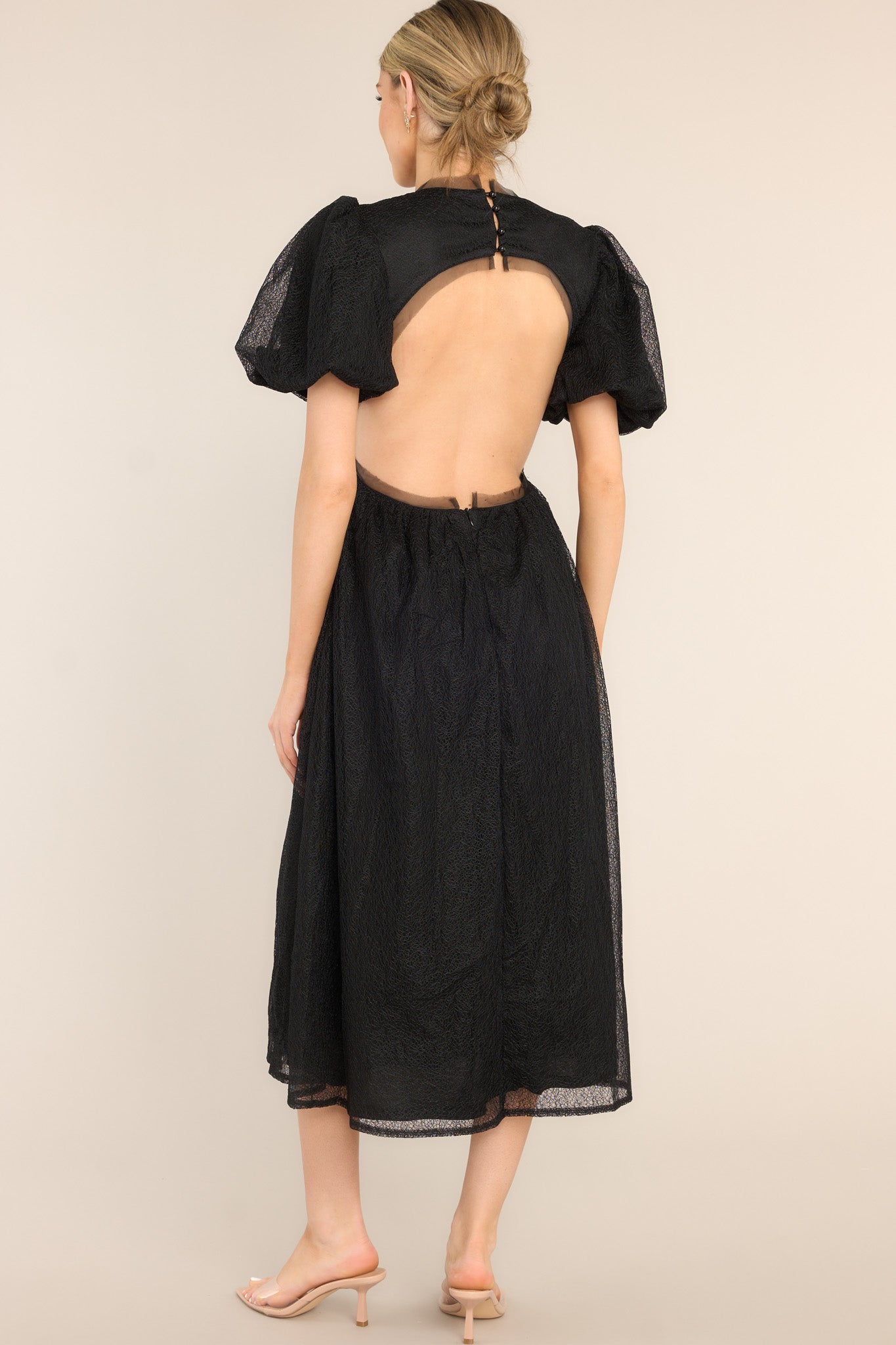 Back view of this midi dress that features a round tulle neckline, short puff sleeves, an open back with a four button closure, and a tulle flowy skirt.