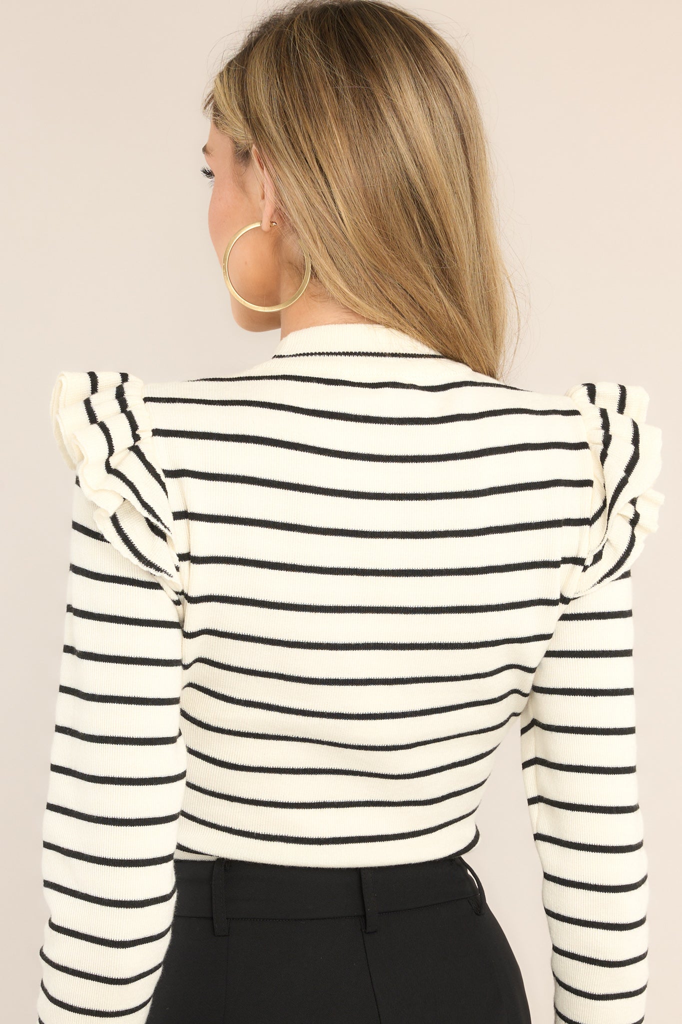 Back view of this bodysuit that features a high neckline, ruffled shoulders, a snap closure, and long sleeves.