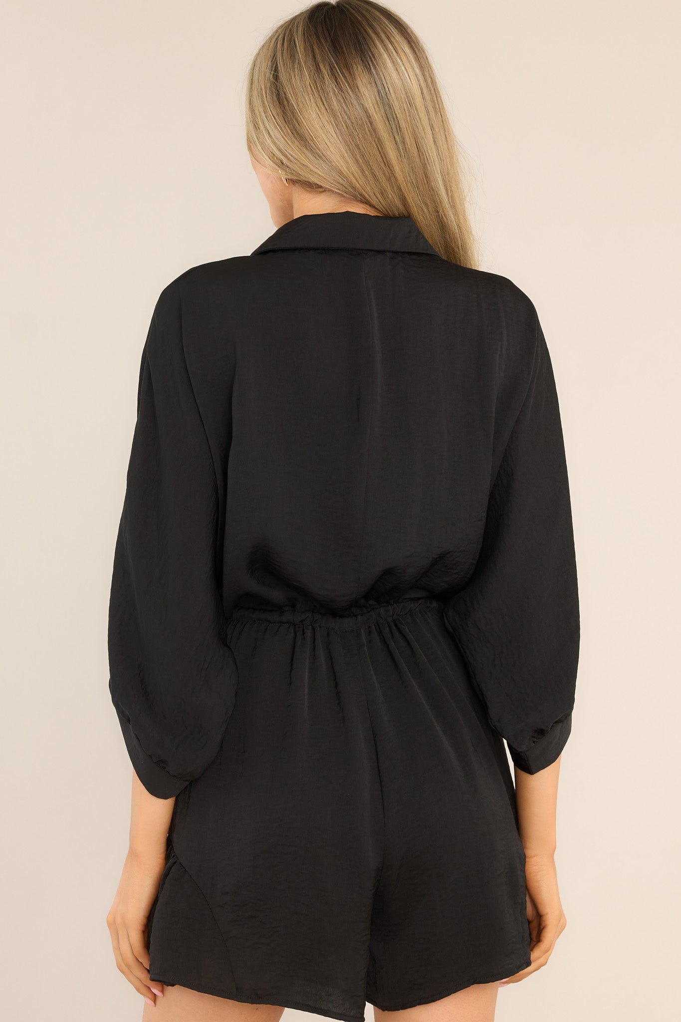 Back view of this romper that features a collared neckline, functional buttons down the front, a self-tie drawstring waist, a lining underneath the shorts, and 3/4 length sleeves.