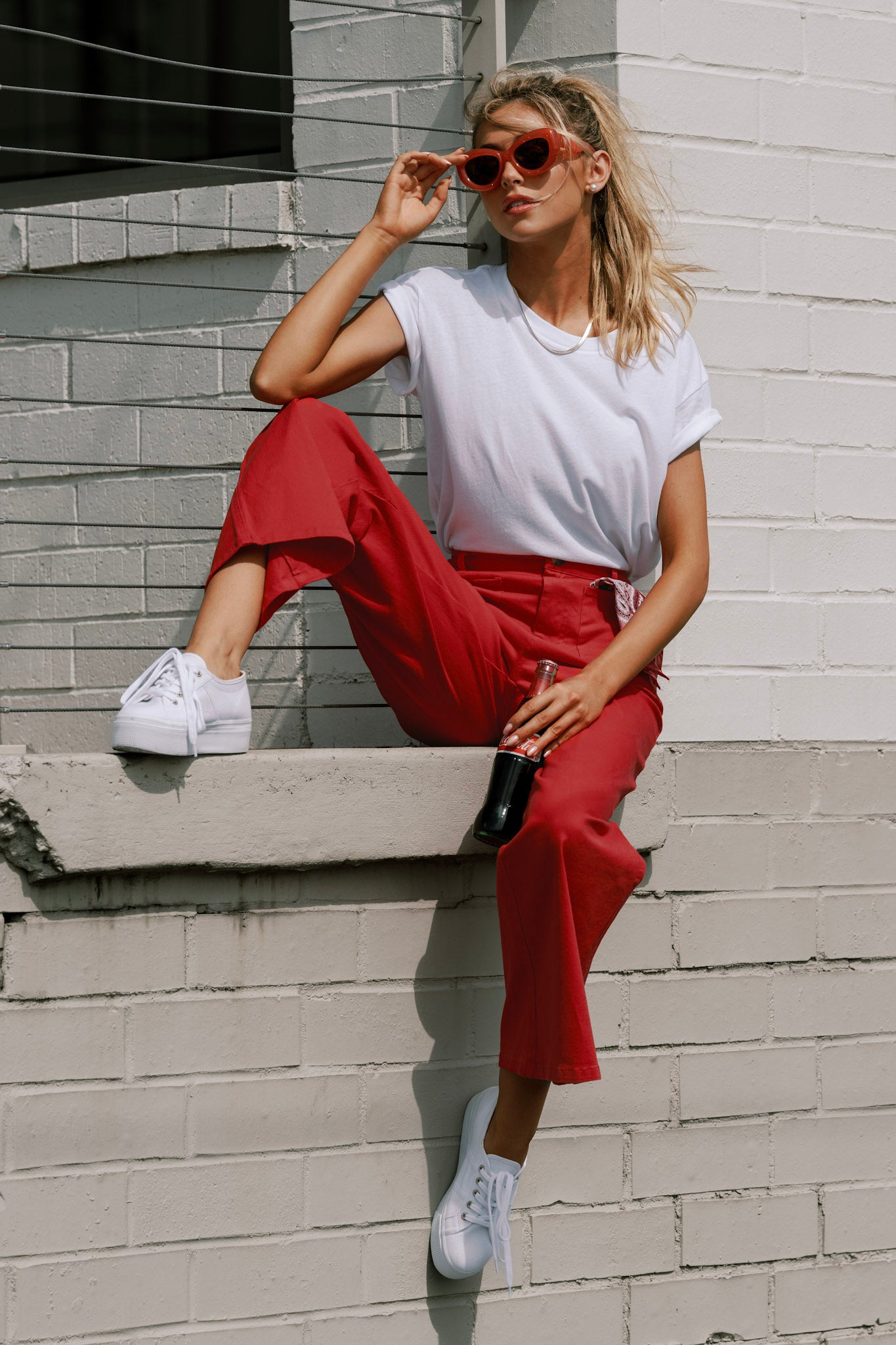 Seated full body view of red pants featuring a high waisted design, classic button & zipper closure, belt loops, functional front pockets, faux back pockets, and a wide leg design.