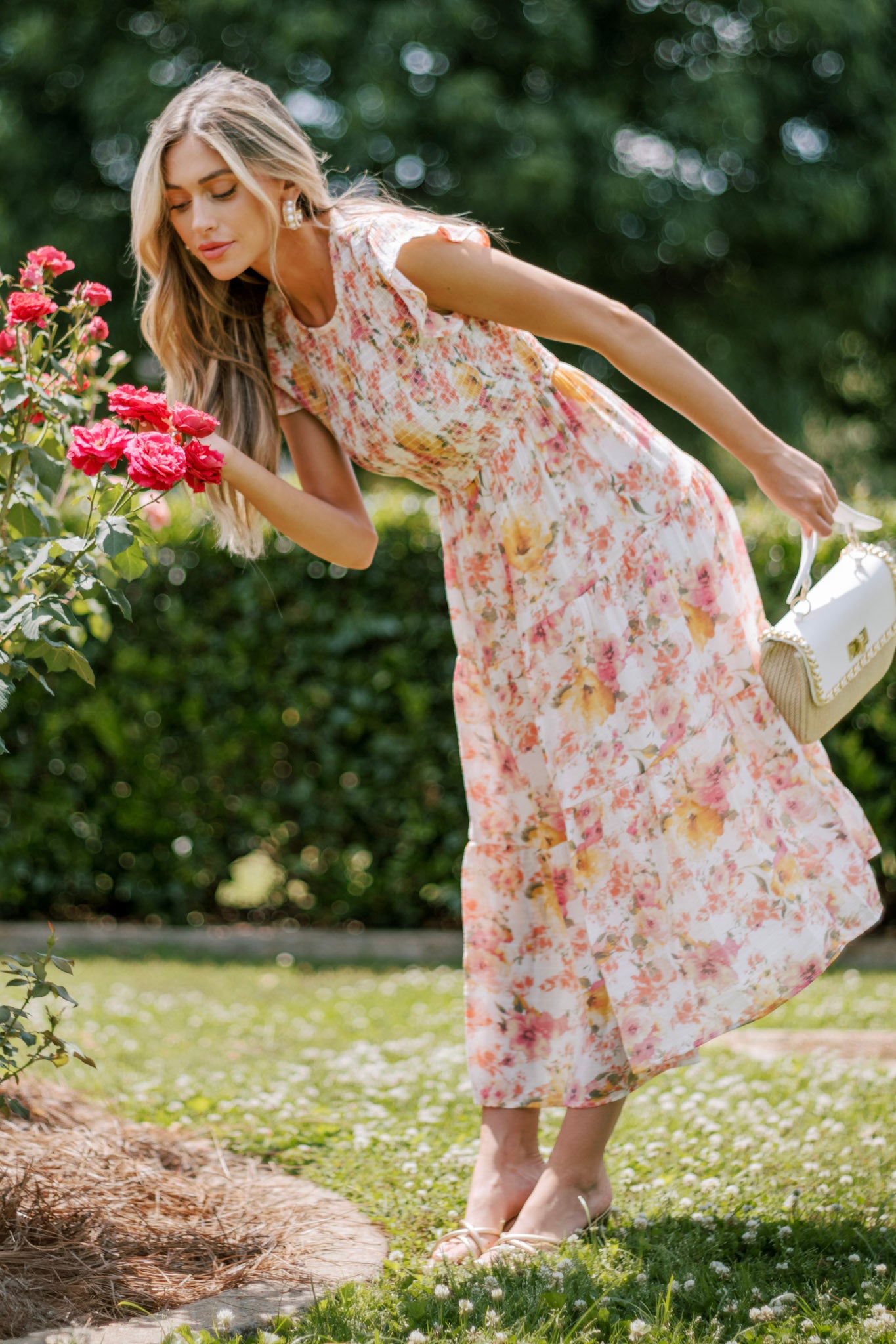 This pink floral midi dress features a high neckline, flutter sleeves, a fully smocked bodice, a tiered design, and a colorful floral pattern.