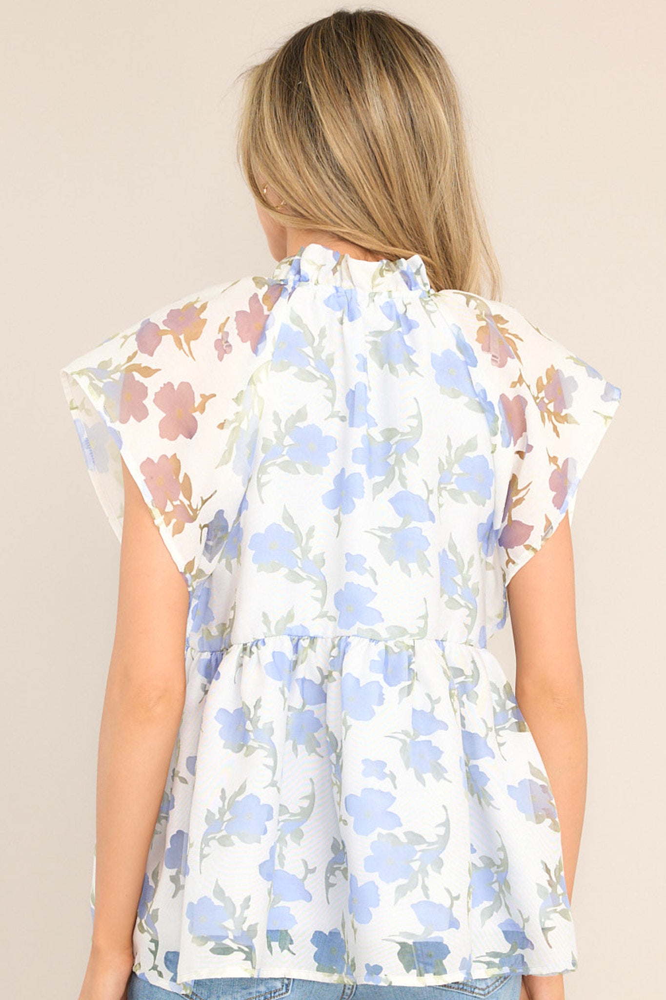 Back view of this top that features a ruffled v-neckline, a flared waistline, wide transparent sleeves, and a delicate floral pattern.