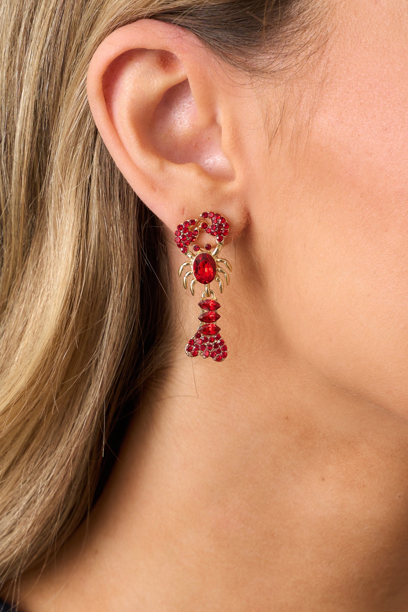 A detailed shot of the lobster-shaped earrings, emphasizing the red rhinestones on the bodice, claws, and tail, along with the secure back postings.