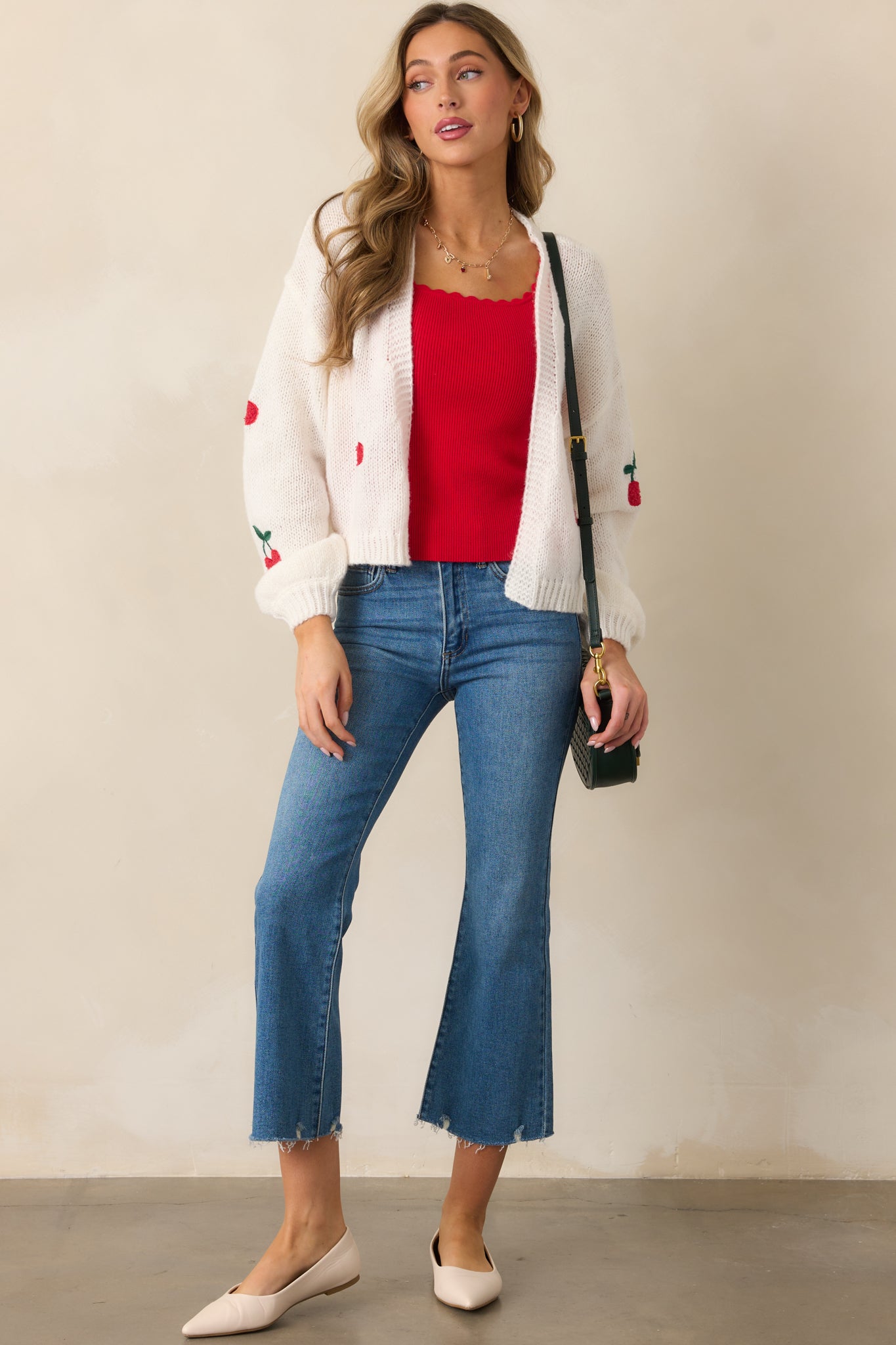 An ivory cardigan with a ribbed open front design, cherry embroidered decals scattered across the front, and long sleeves.