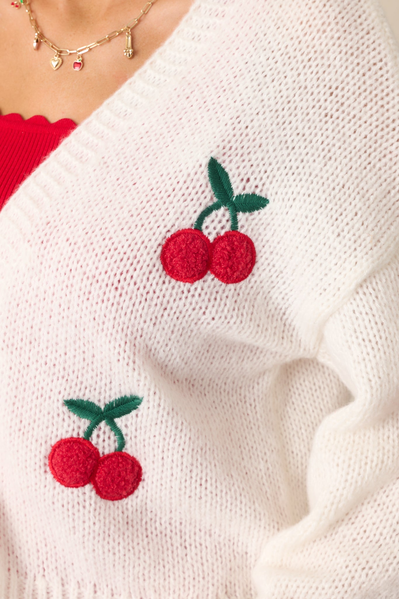 A detailed shot of the cherry embroidered decals, showing the stitching and texture against the ribbed ivory fabric.