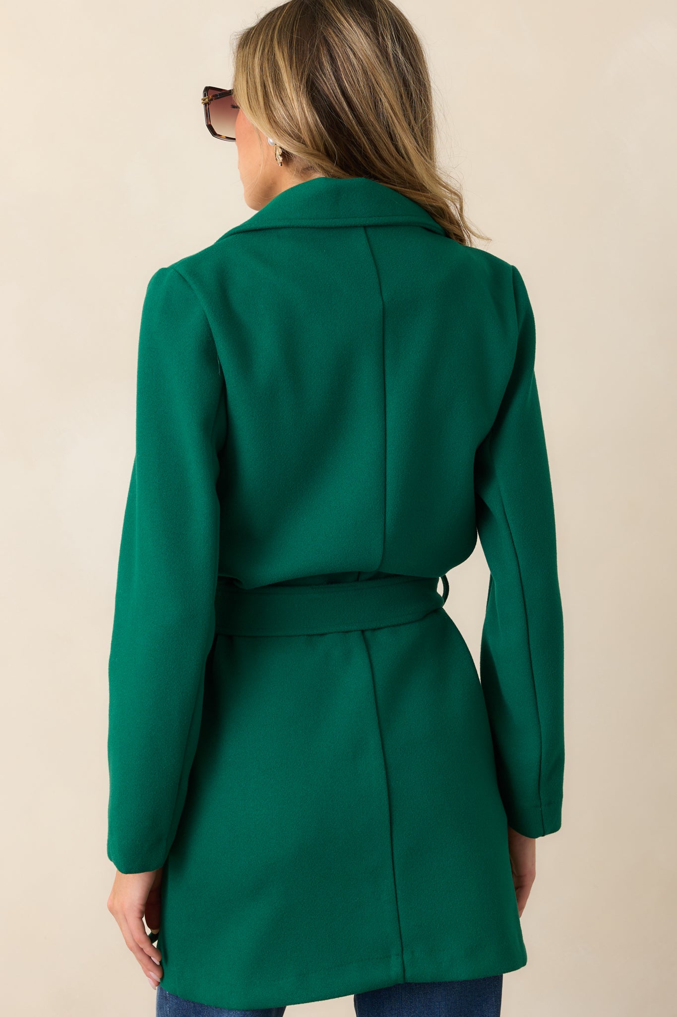 The back view of the kelly green coat, showcasing the clean lines, long sleeves, and the tie detail visible from the back.