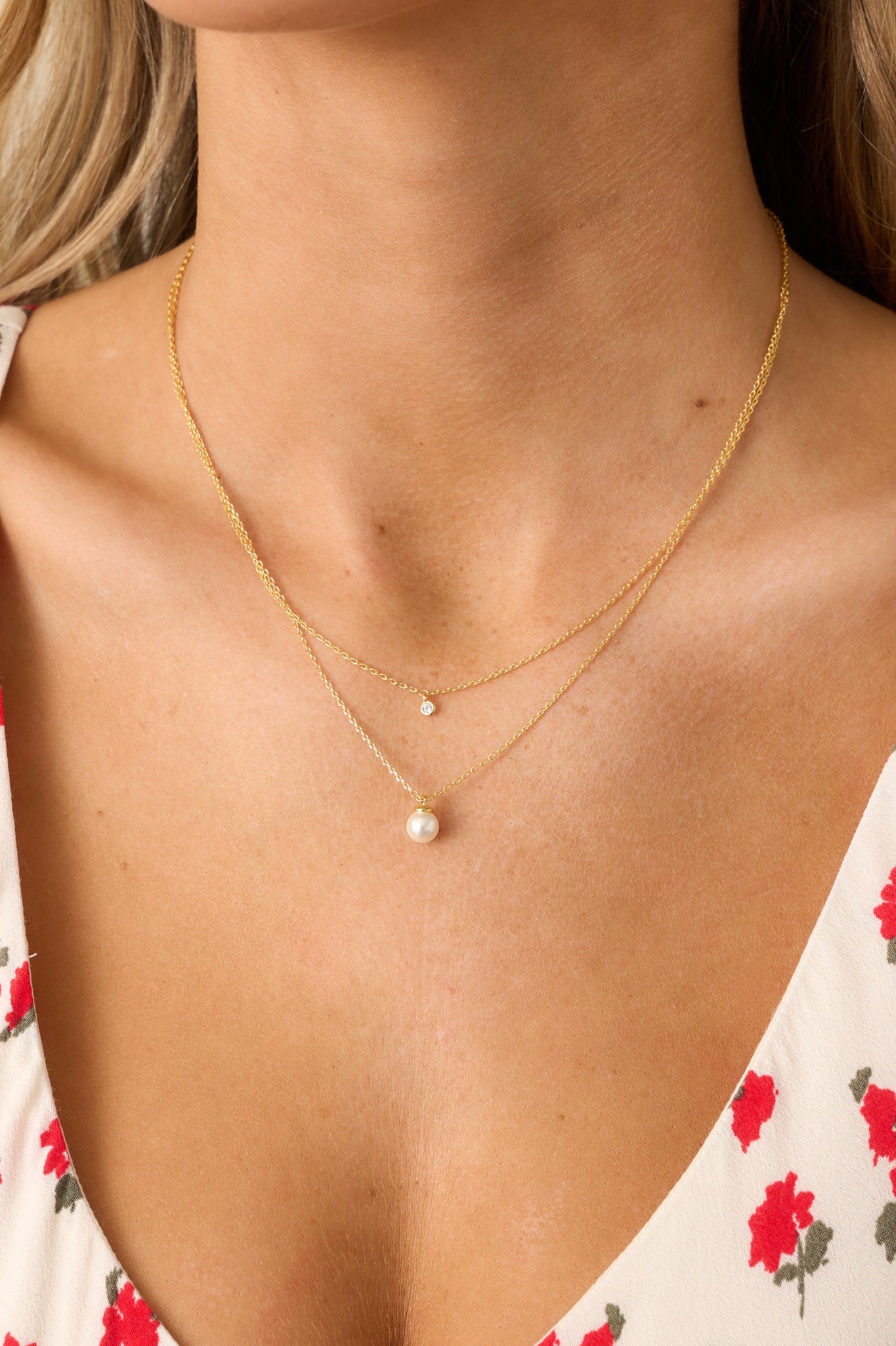 A close view of the gold necklace highlighting the layered design, with the shorter chain featuring a small rhinestone pendant.