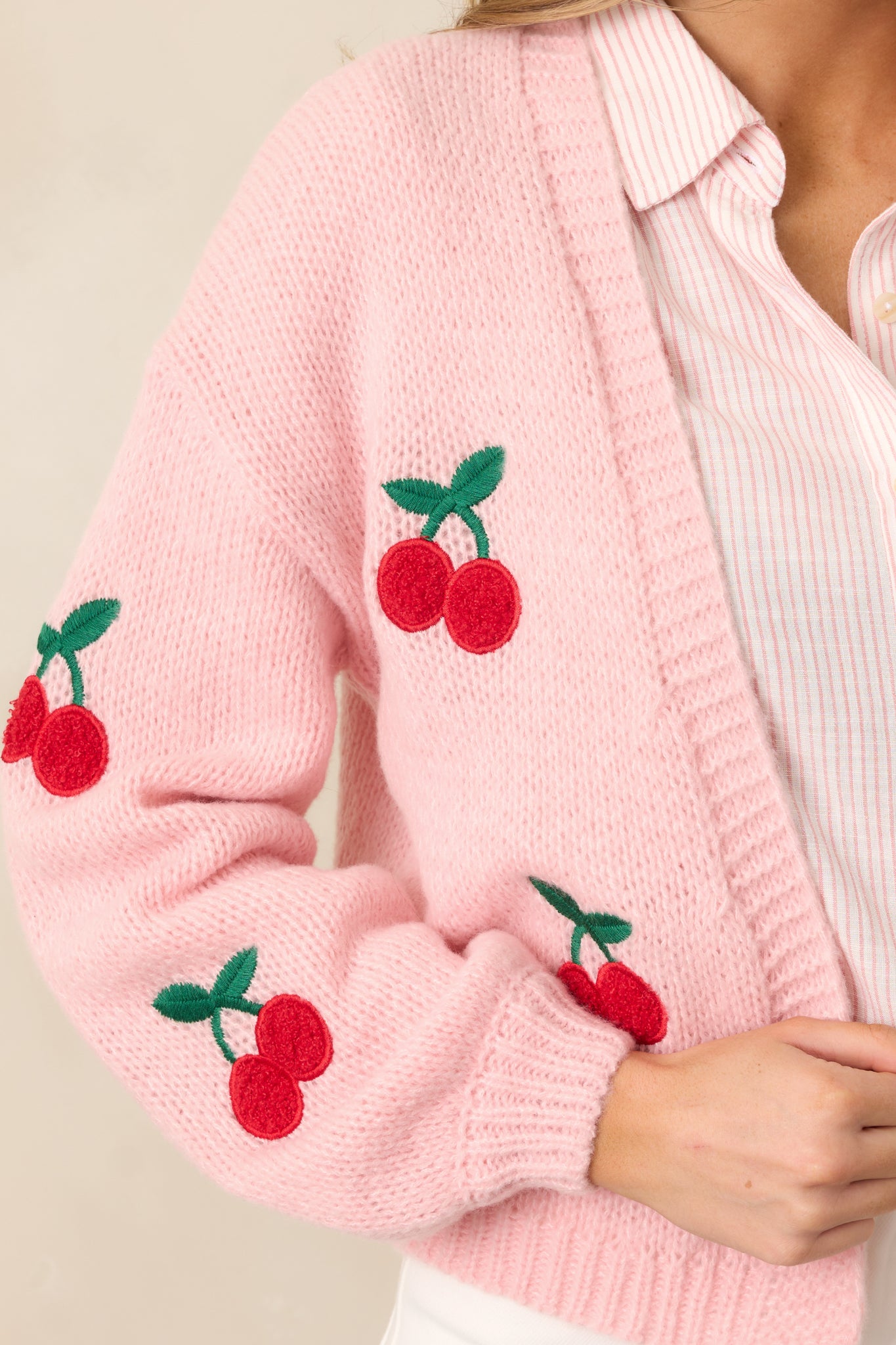 A focus on the sleeve of the pink cardigan, capturing the cherry embroidery and ribbed cuffs in detail.