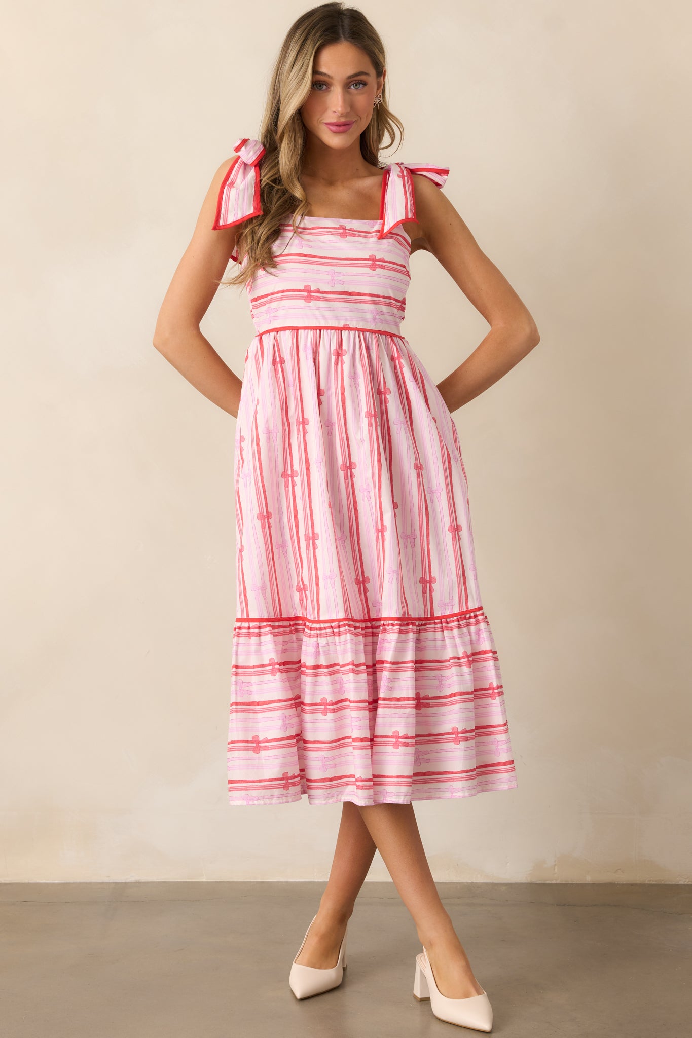 The pink dress shown from the front, highlighting the square neckline, red trim, and tiered skirt with the delicate bow stripe print.