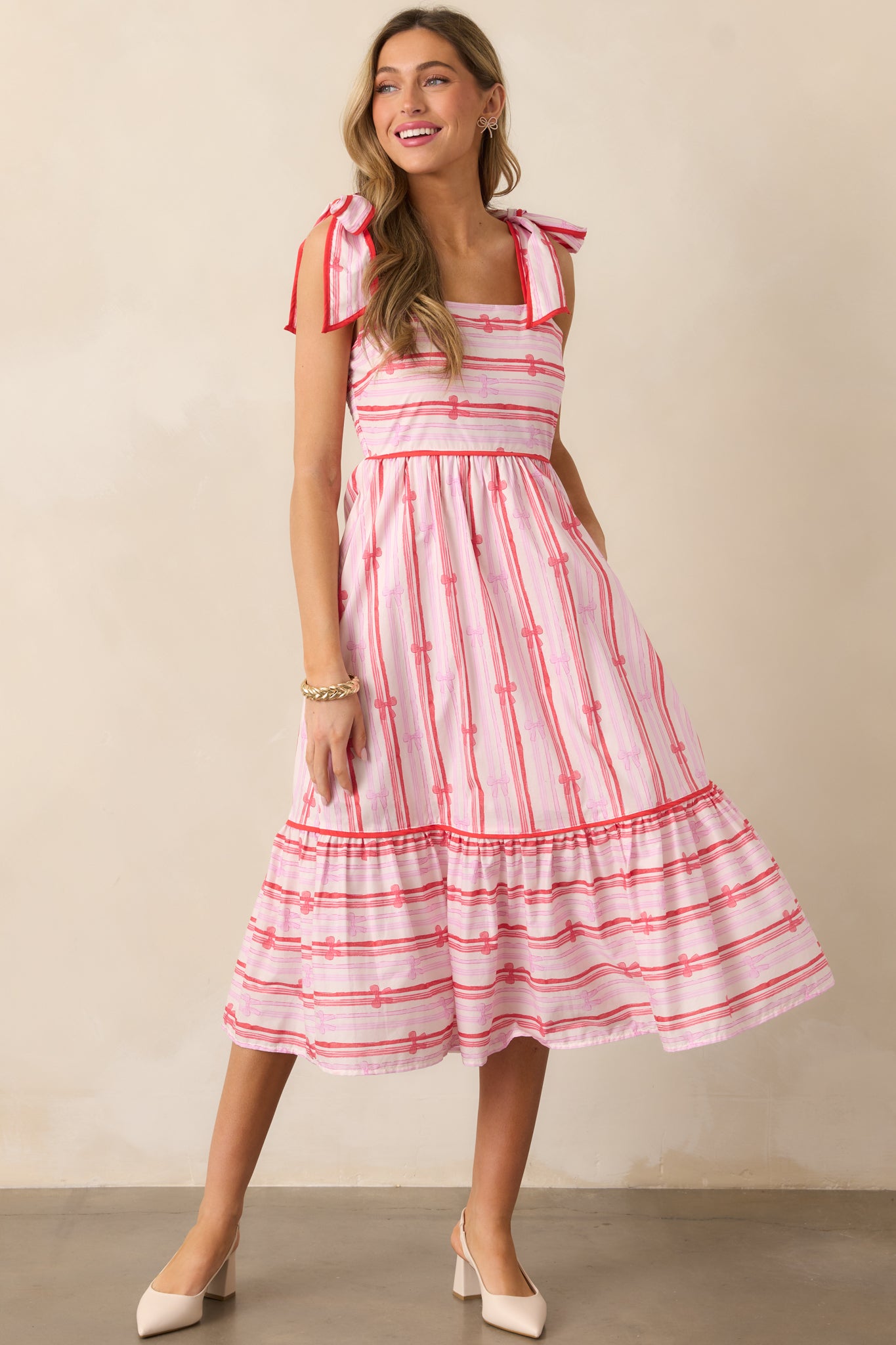 A slight angle of the pink dress showcasing its tiered bottom, bow stripe print, and the contrast of the red trim on the neckline and shoulder straps.