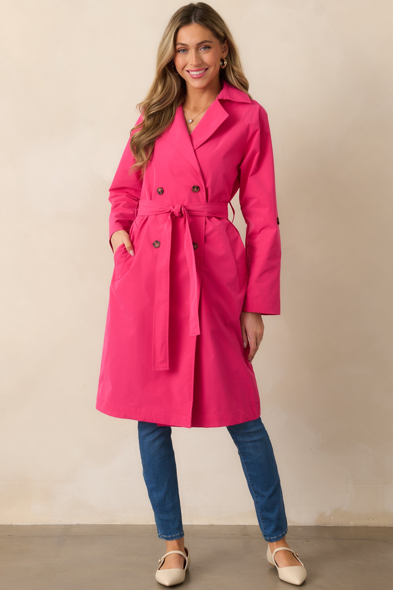 A full view of the magenta coat featuring a collared neckline, double-breasted lapel design, self-tie waistband, and long sleeves with functional pockets.