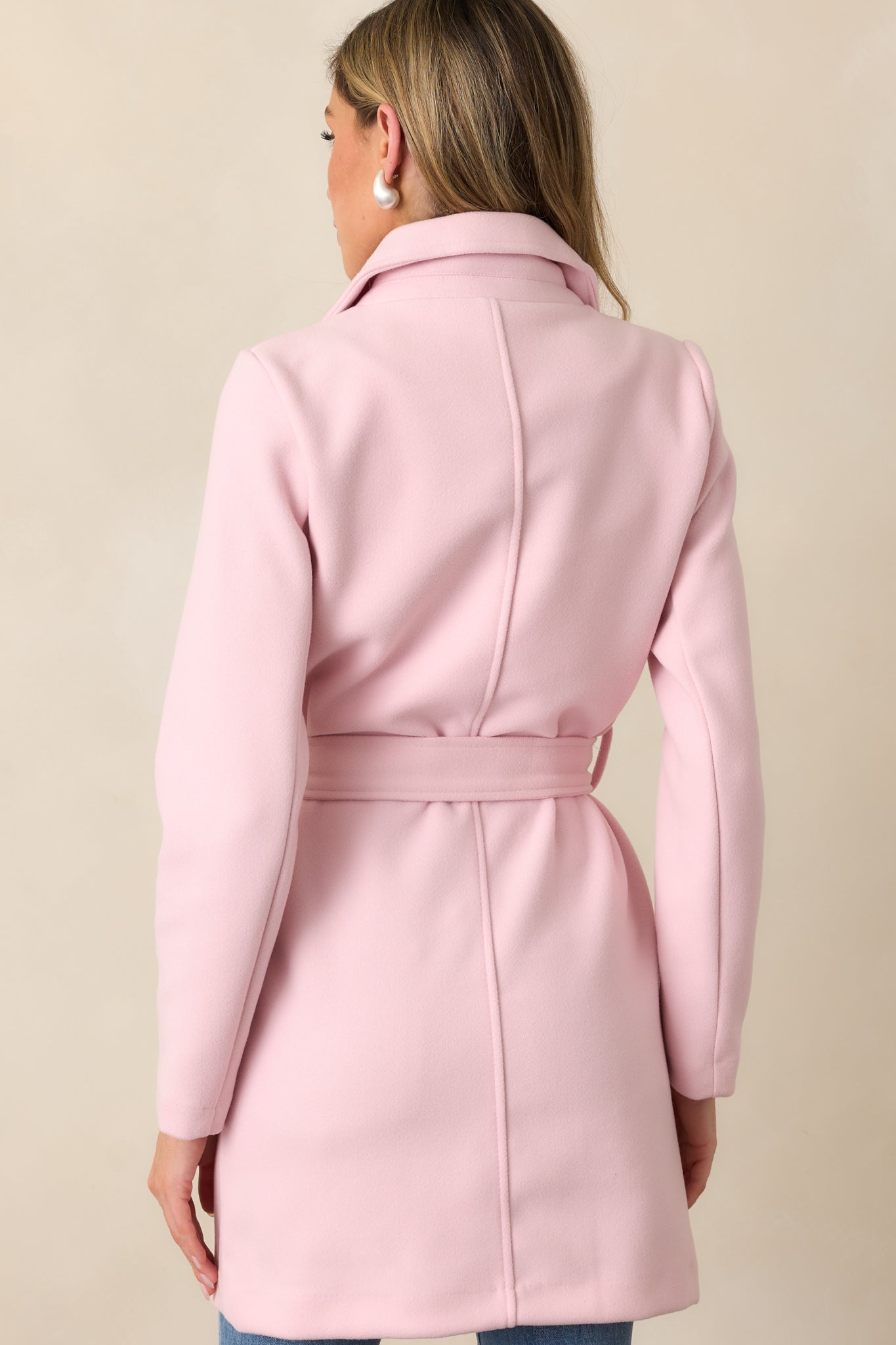 A back view of the light pink coat, featuring the tied waistband and the clean lines of the back design.