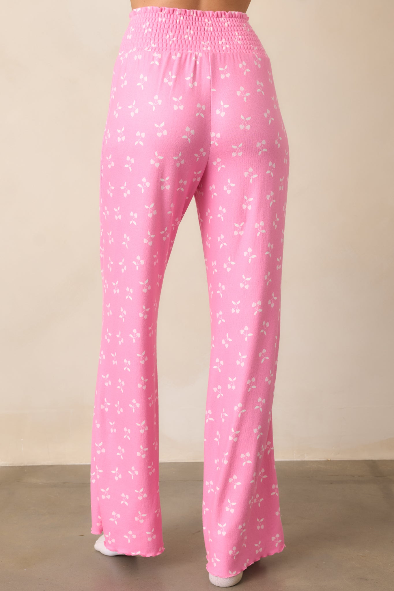 The back of the pink pants, emphasizing the relaxed fit, smocked waistband, and continuation of the cherry print and lettuce hem trim.