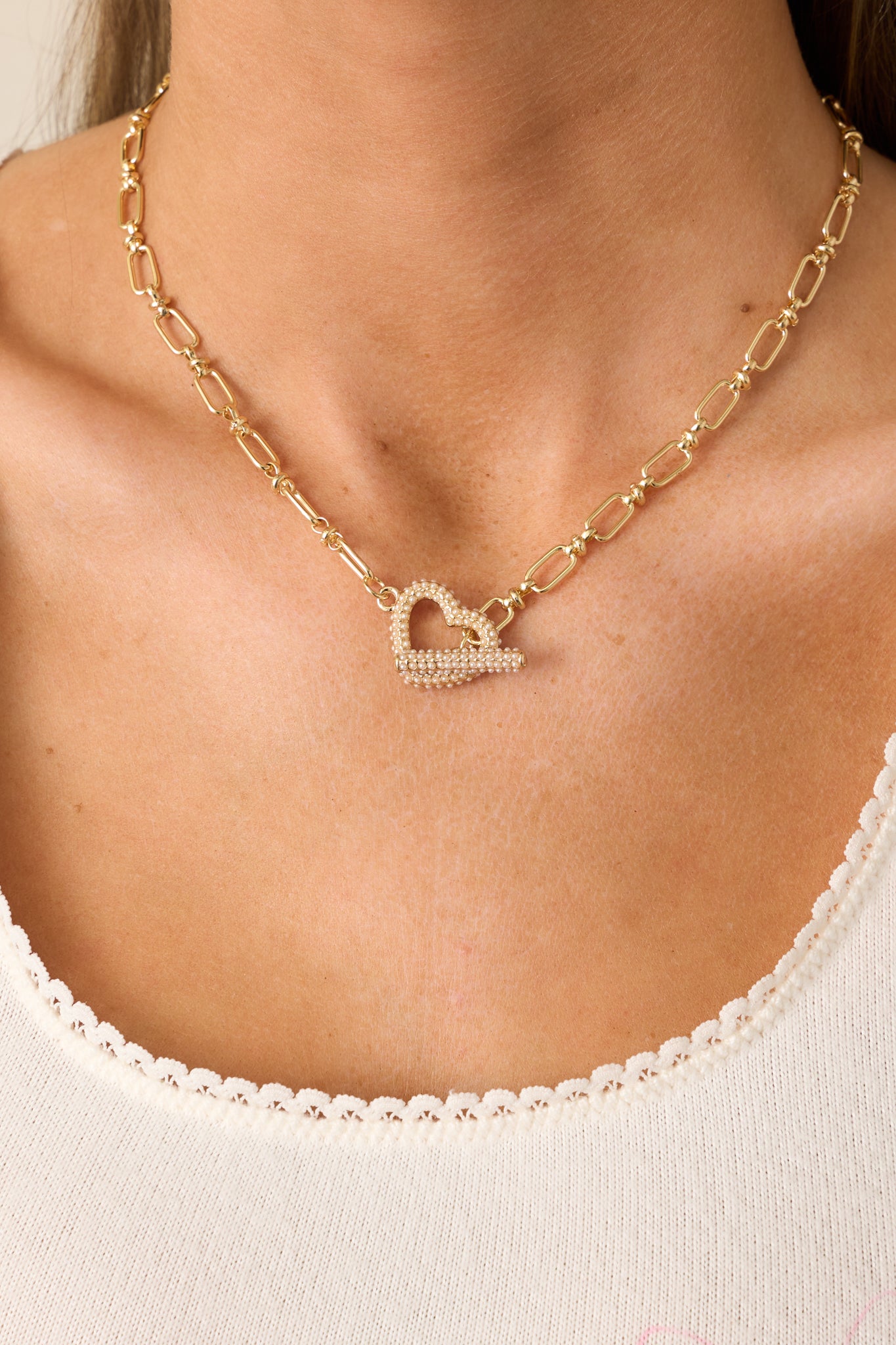 A detailed shot of the gold heart pendant with small faux ivory pearls, emphasizing its design and the thin gold chain.