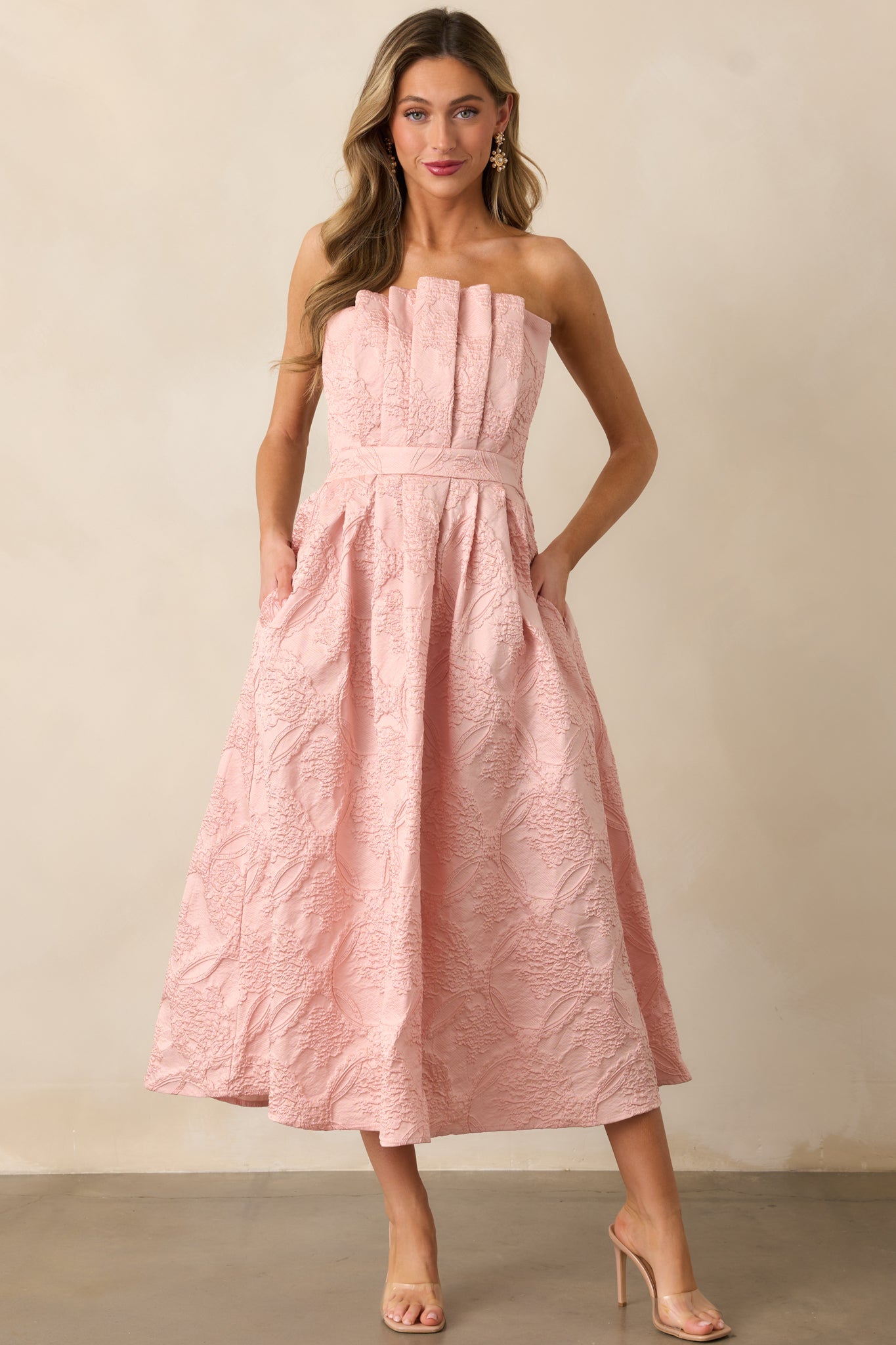 The blush dress shown from the front, highlighting the pleated bodice, smocked back, and the elegant flow of the slightly pleated skirt.