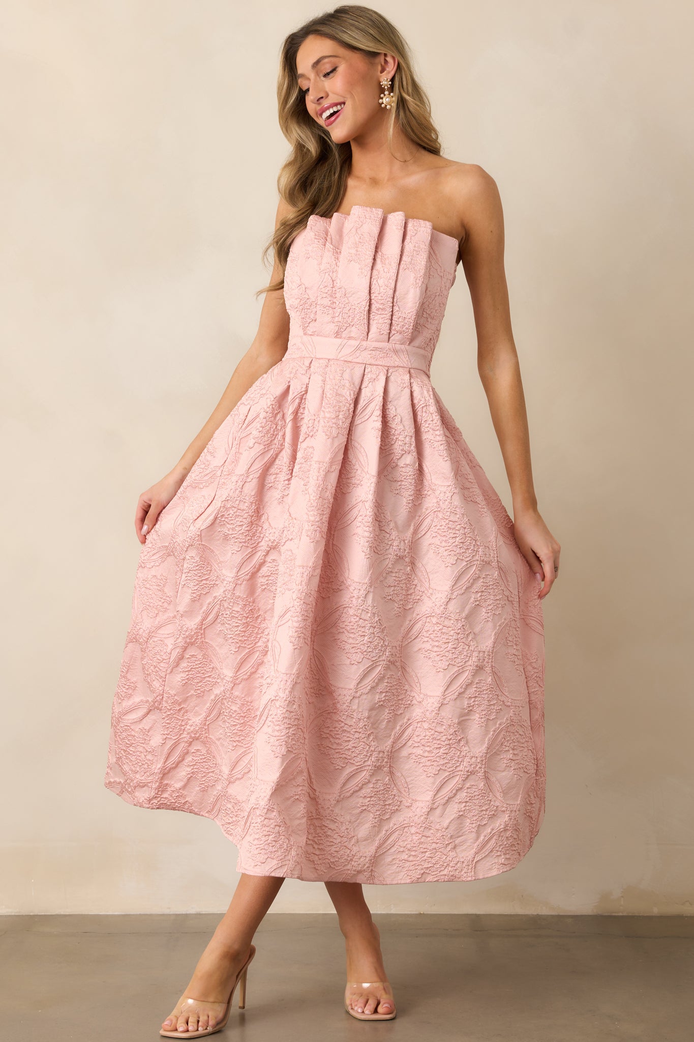 A slight angle of the blush dress showing off the pleated bodice, functional hip pockets, and the gentle pleats of the skirt.