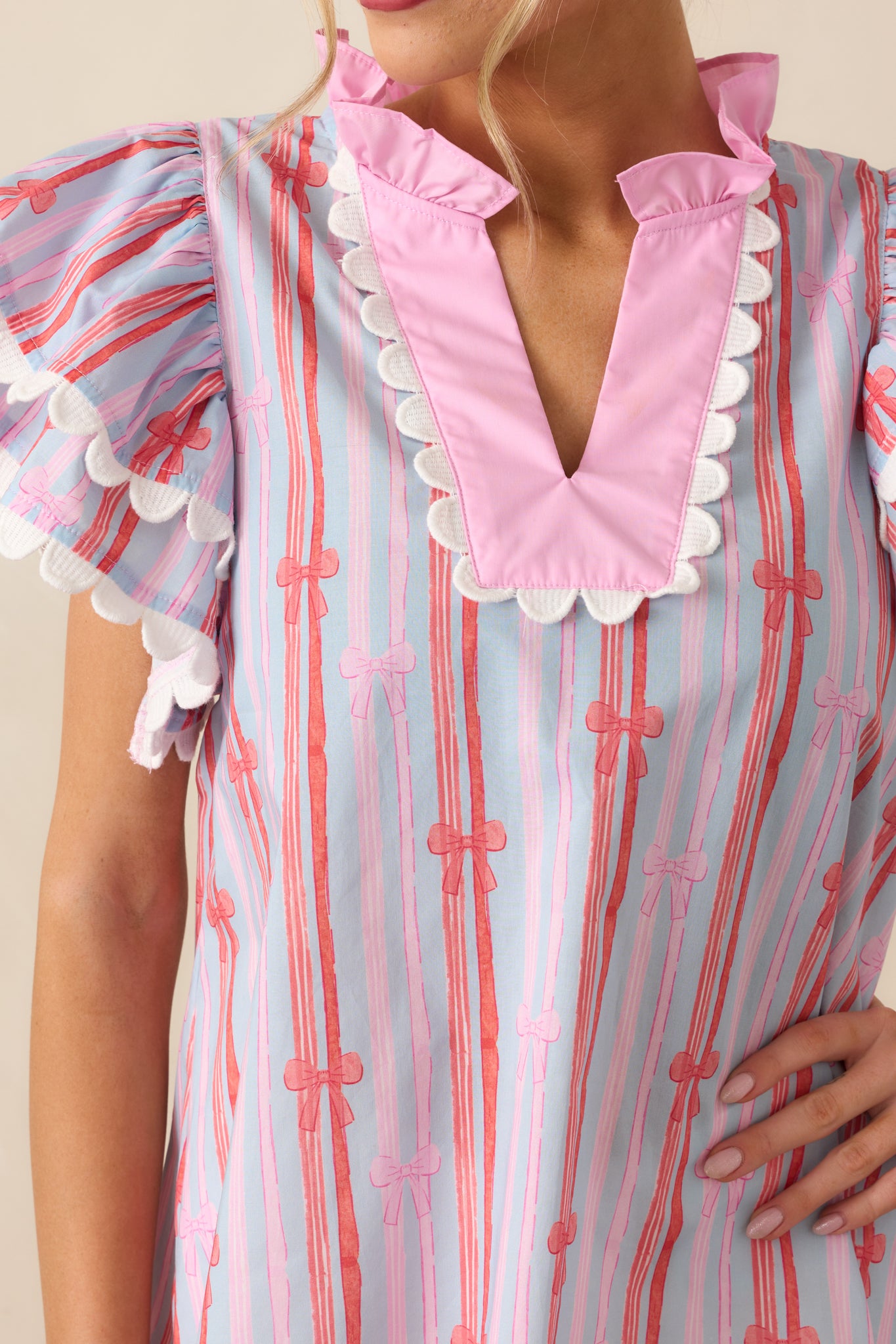 A detailed close-up showing the stripe and bow pattern, the notch neckline, and the scalloped trim of the flutter sleeves.