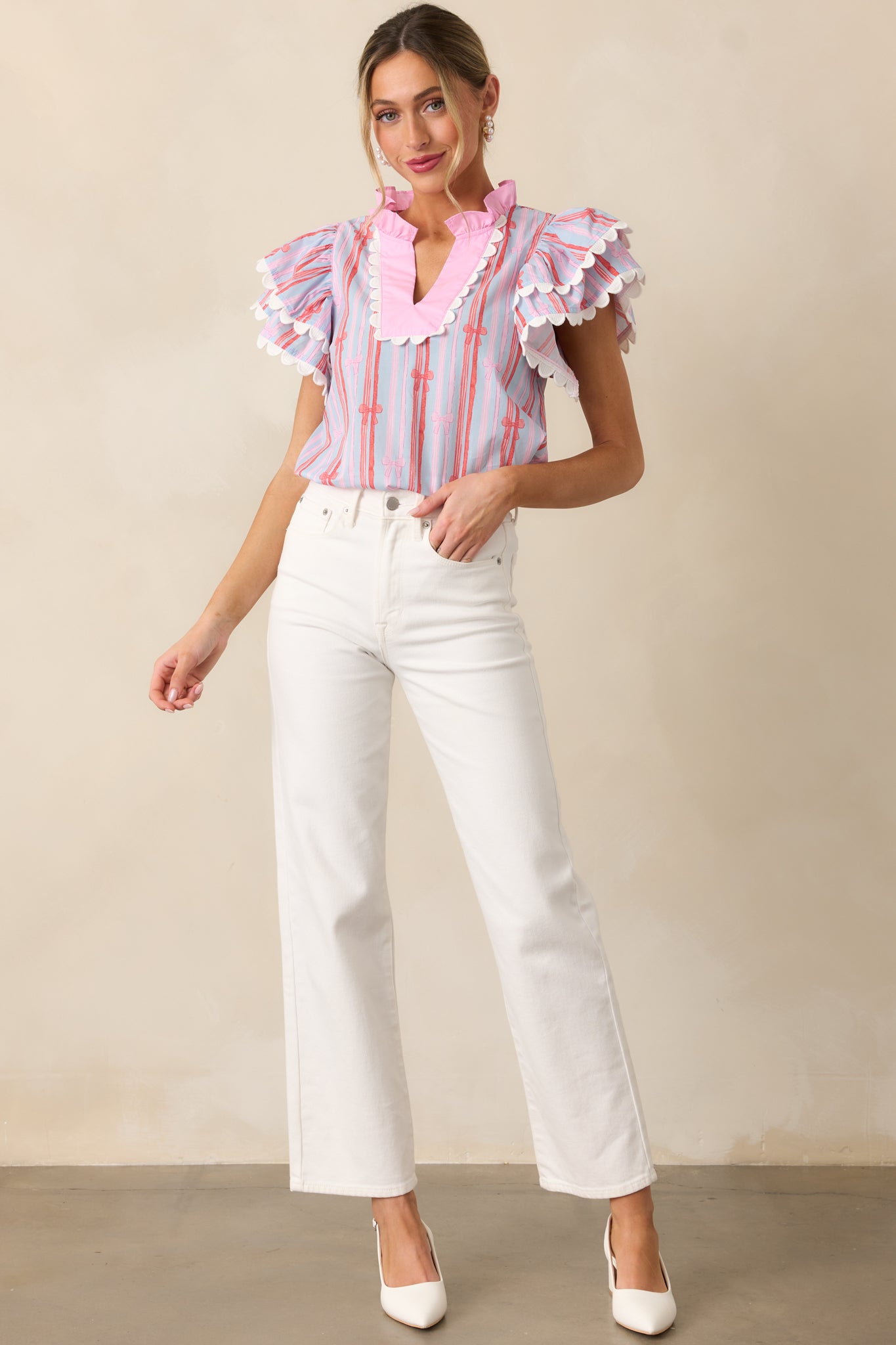 A full view of the light blue blouse featuring a notch neckline, relaxed fit, stripe and bow pattern, and double flutter sleeves with scalloped trim.