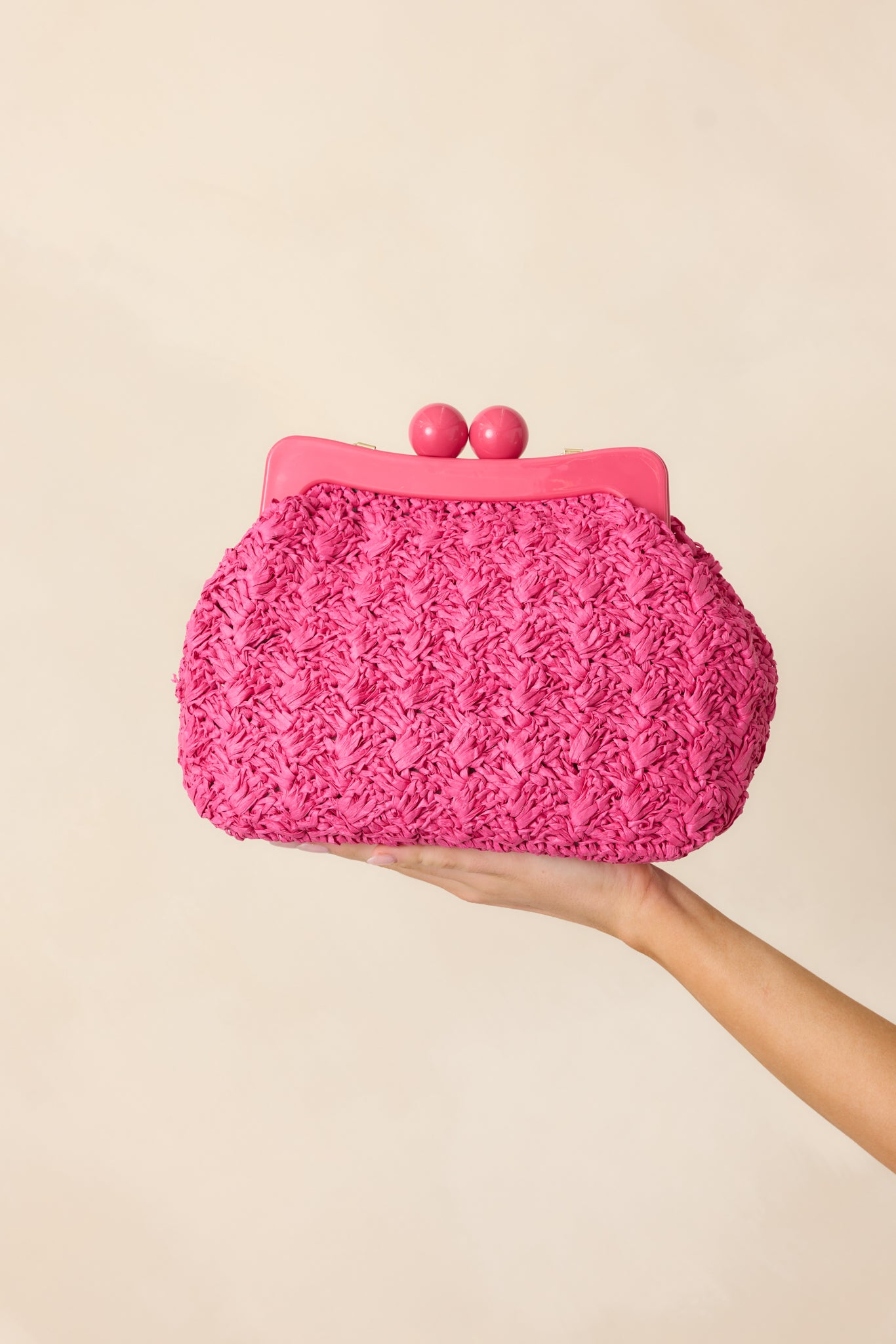 A woven hot pink clutch with a magnetic lined clasp, large ball kiss lock detail, and optional gold chain strap.