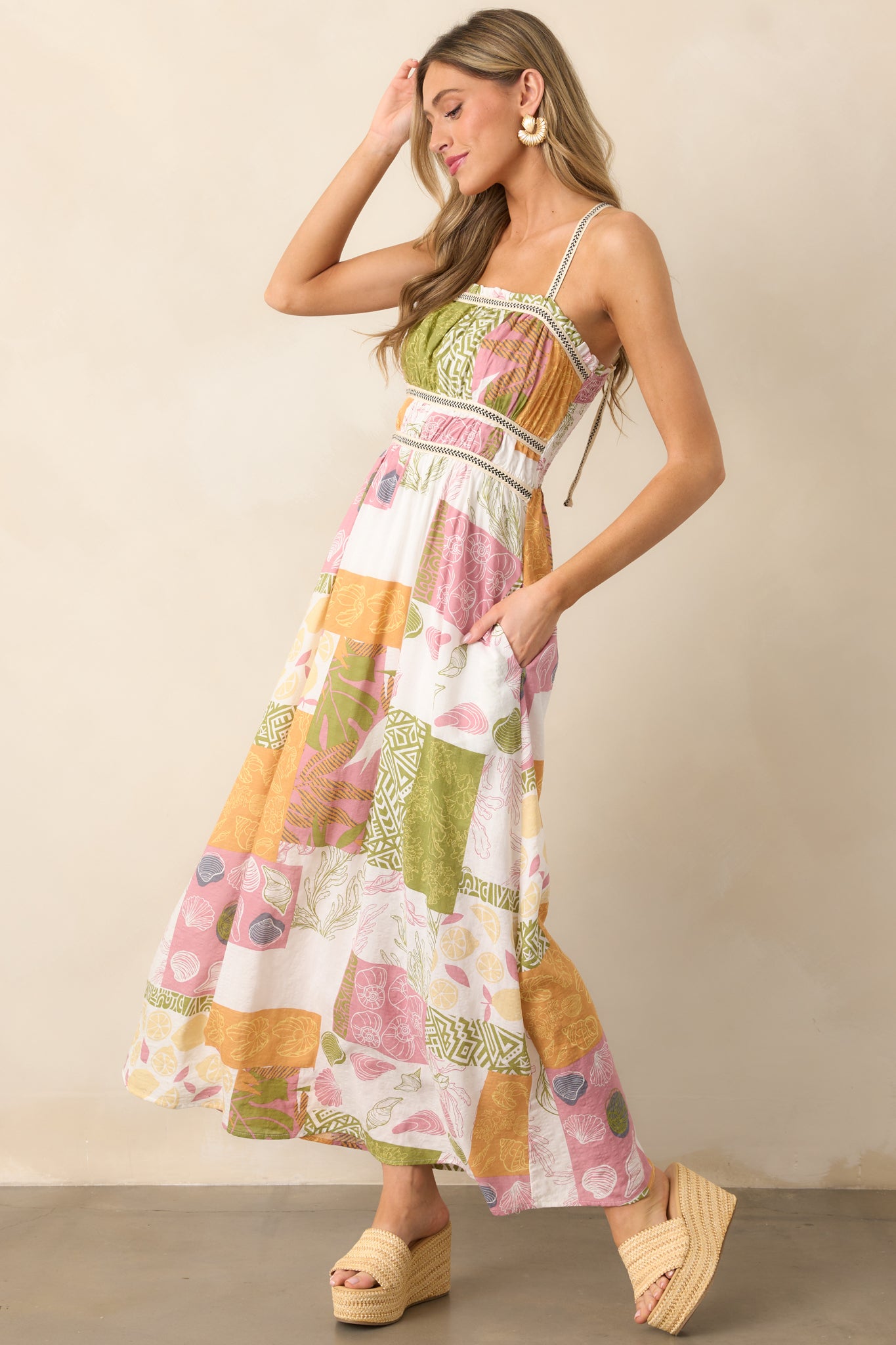 A side view of the dress, emphasizing the cross-back embroidered shoulder straps, ruffle neckline, and the flow of the tropical patchwork design on the maxi-length skirt.