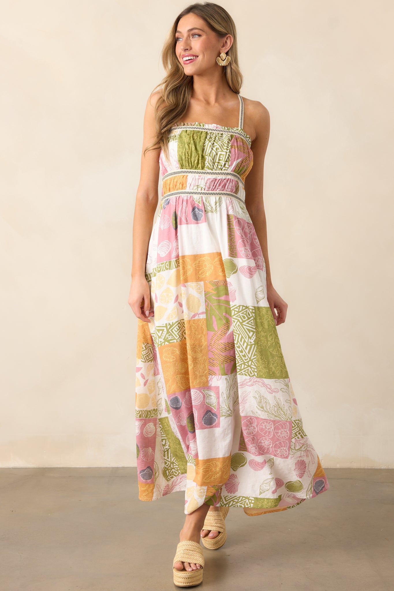 A full view of the ivory maxi dress showcasing its straight neckline with ruffle detail, smocked back, tropical patchwork design, and cross-back embroidered shoulder straps.