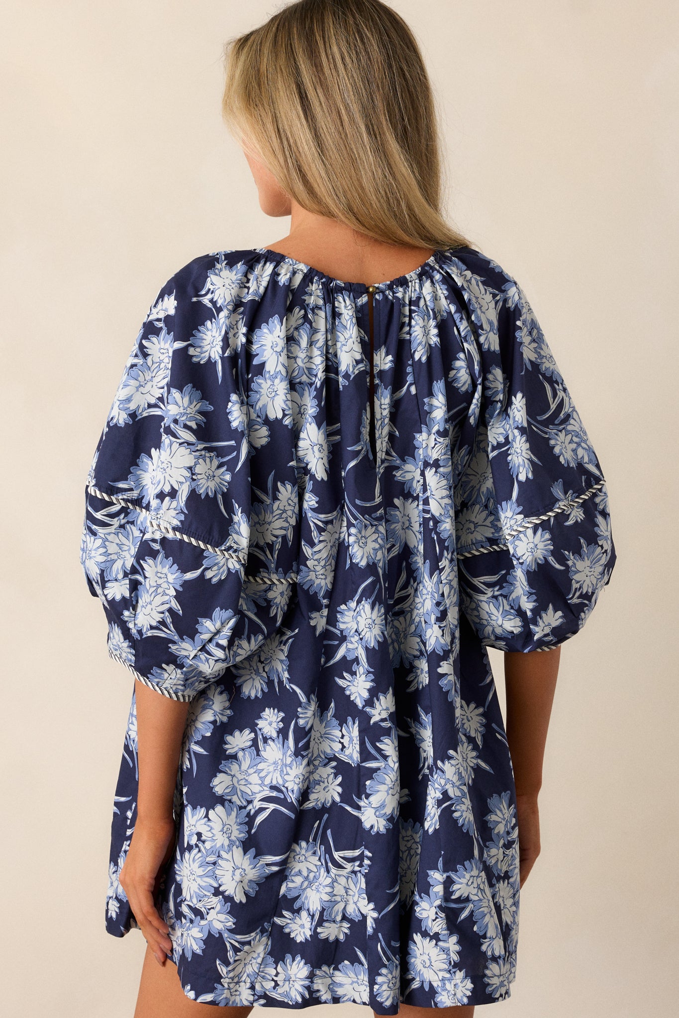 Back view of the navy floral romper, displaying the relaxed fit, half-length balloon sleeves, and uninterrupted floral pattern flowing down to the hem.