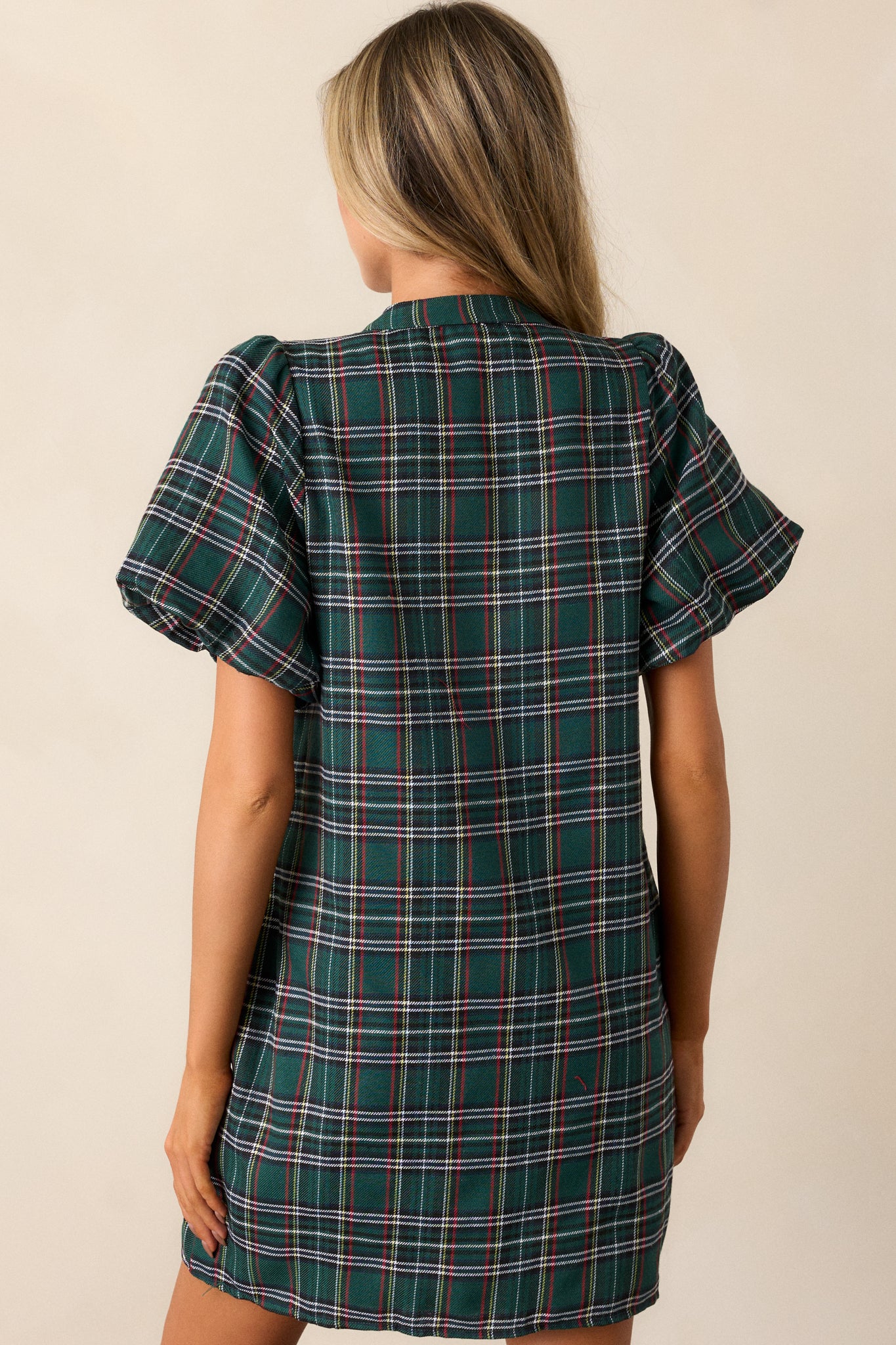 Back view of a green mini dress featuring a v-neckline, plaid design, black sequin bow detailing, and puff sleeves with elastic cuffs.