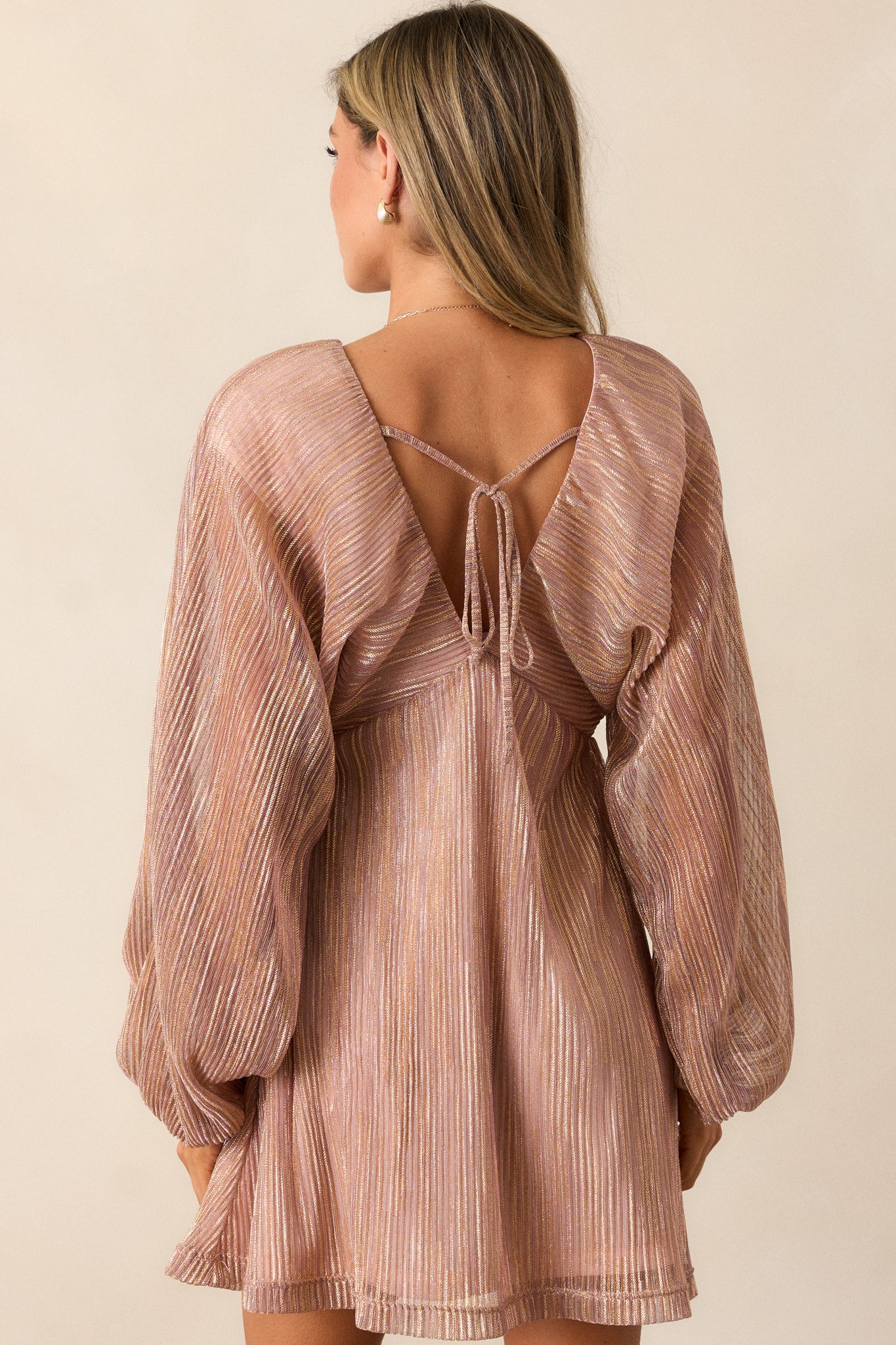 Back view of the rose gold mini dress, displaying the dainty tie detail and the flowing silhouette of the balloon sleeves from behind.