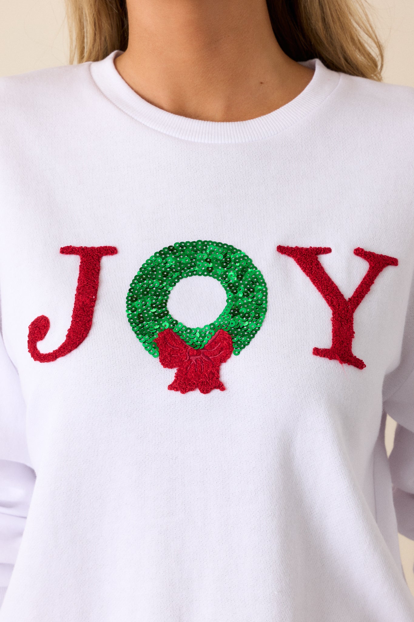 Close up of embroidered and sequin "JOY" on a white, long sleeve sweatshirt.