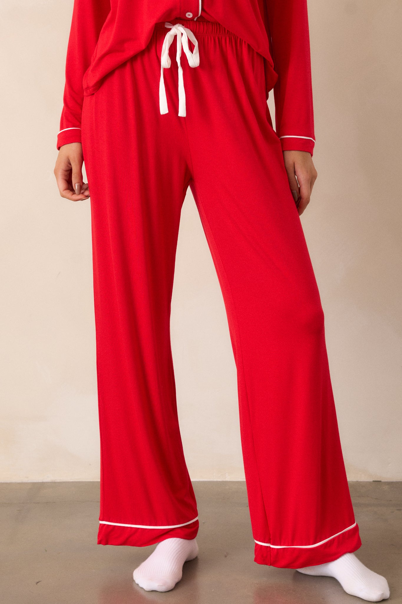 Close up view of red Pajama Pants featuring an elastic drawstring waistband with a white string, white trim detailing and long relaxed pant legs.