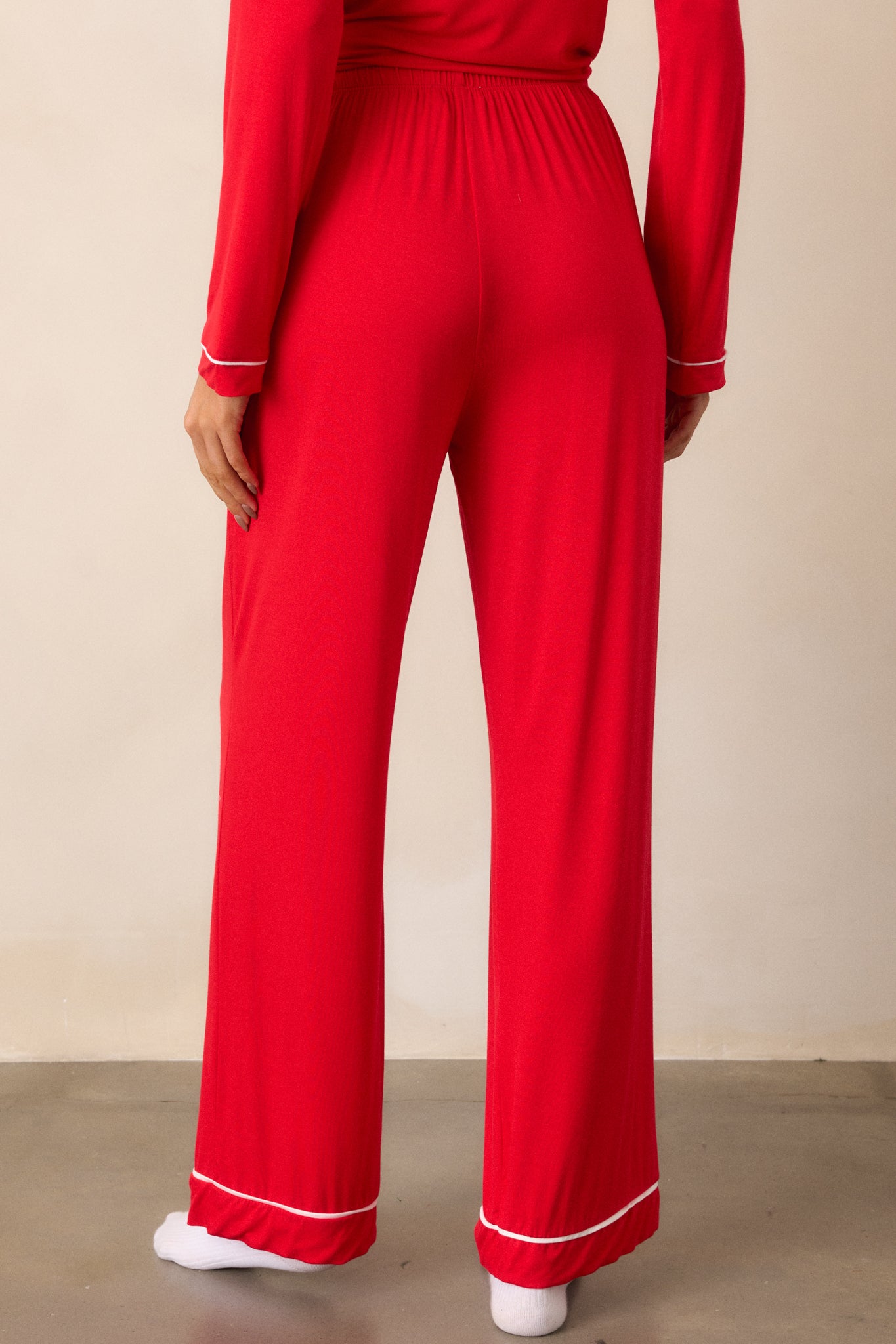 Back view of red Pajama Pants featuring an elastic drawstring waistband with a white string, white trim detailing and long relaxed pant legs.