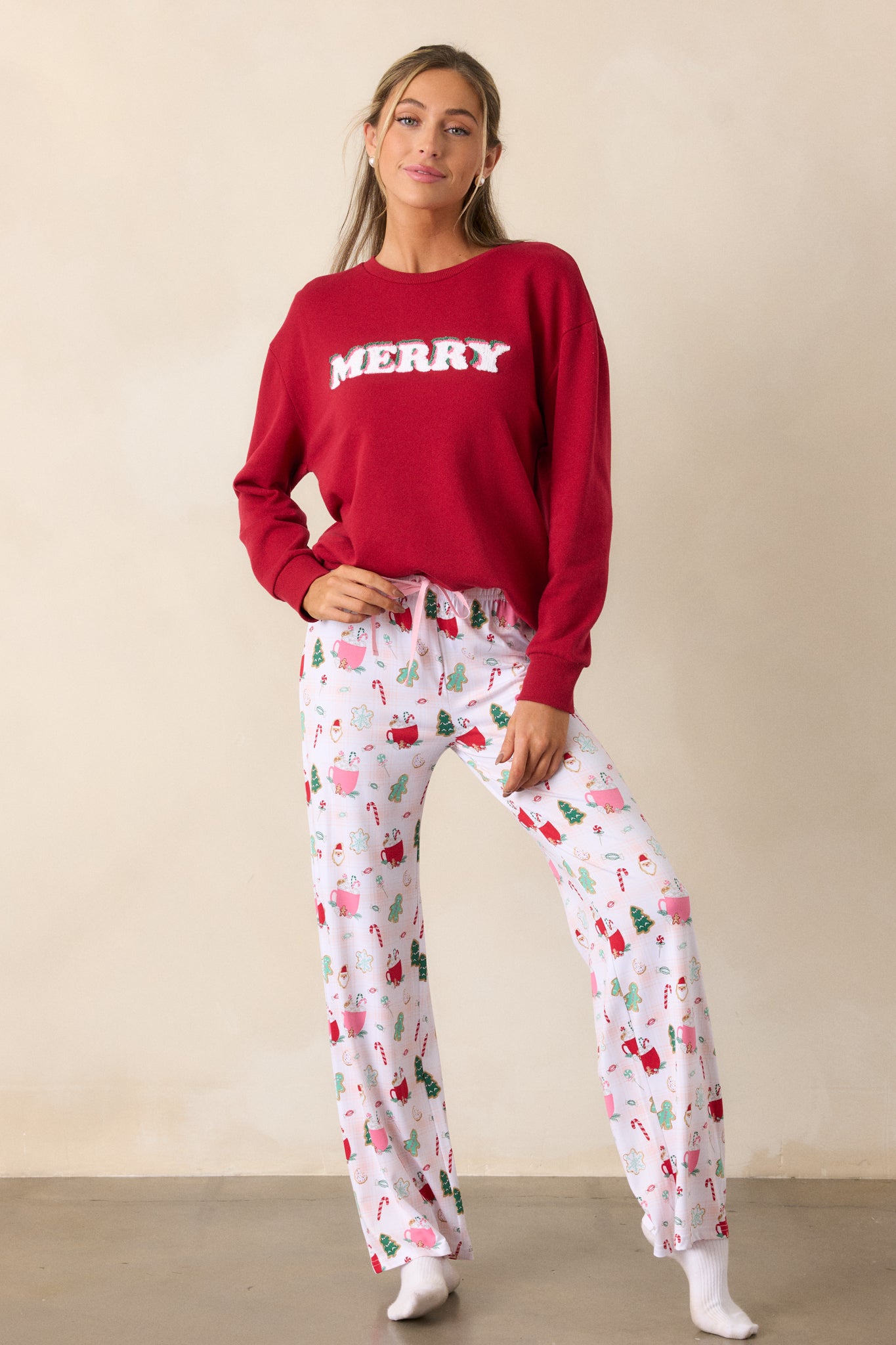 A full view of the ivory pajama pants, highlighting the elastic drawstring waistband with a pink string and the fun holiday hot cocoa and treats print throughout the relaxed pant legs.