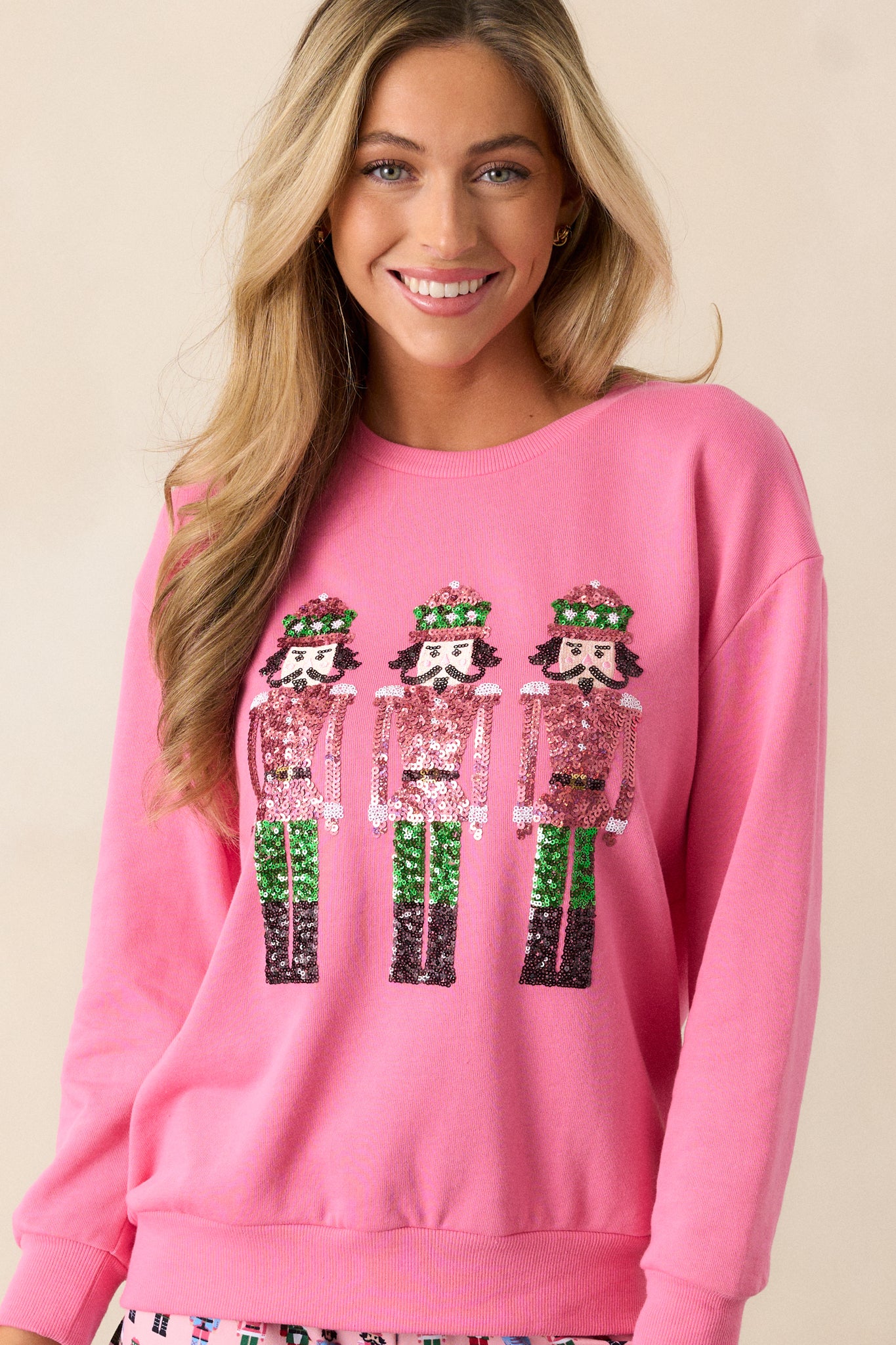 Front view of a pink sweatshirt featuring a crew neckline, sequin nutcracker design, a relaxed fit and long sleeves with ribbed hems.