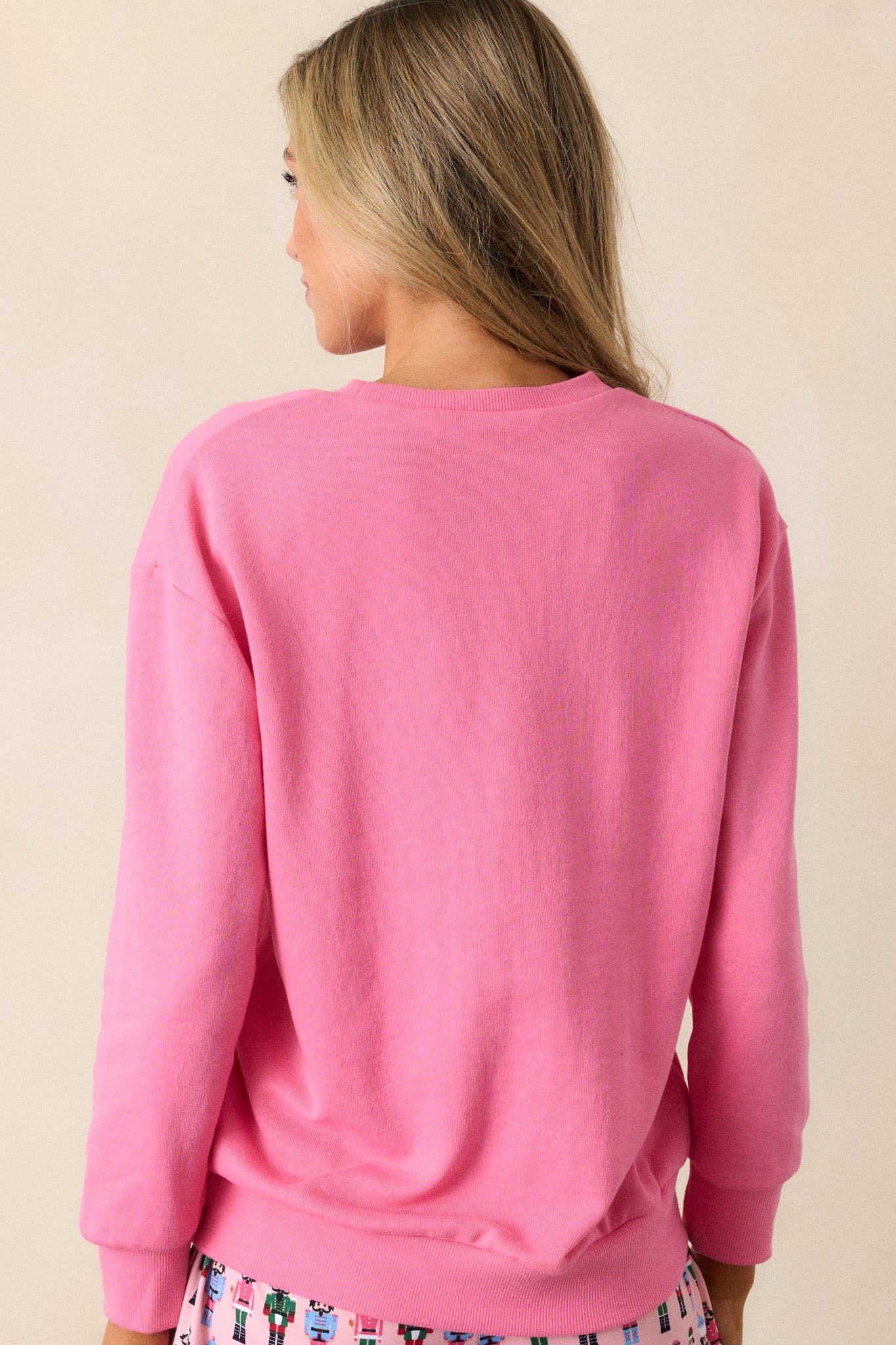 Back view of a pink sweatshirt featuring a crew neckline, sequin nutcracker design, a relaxed fit and long sleeves with ribbed hems.