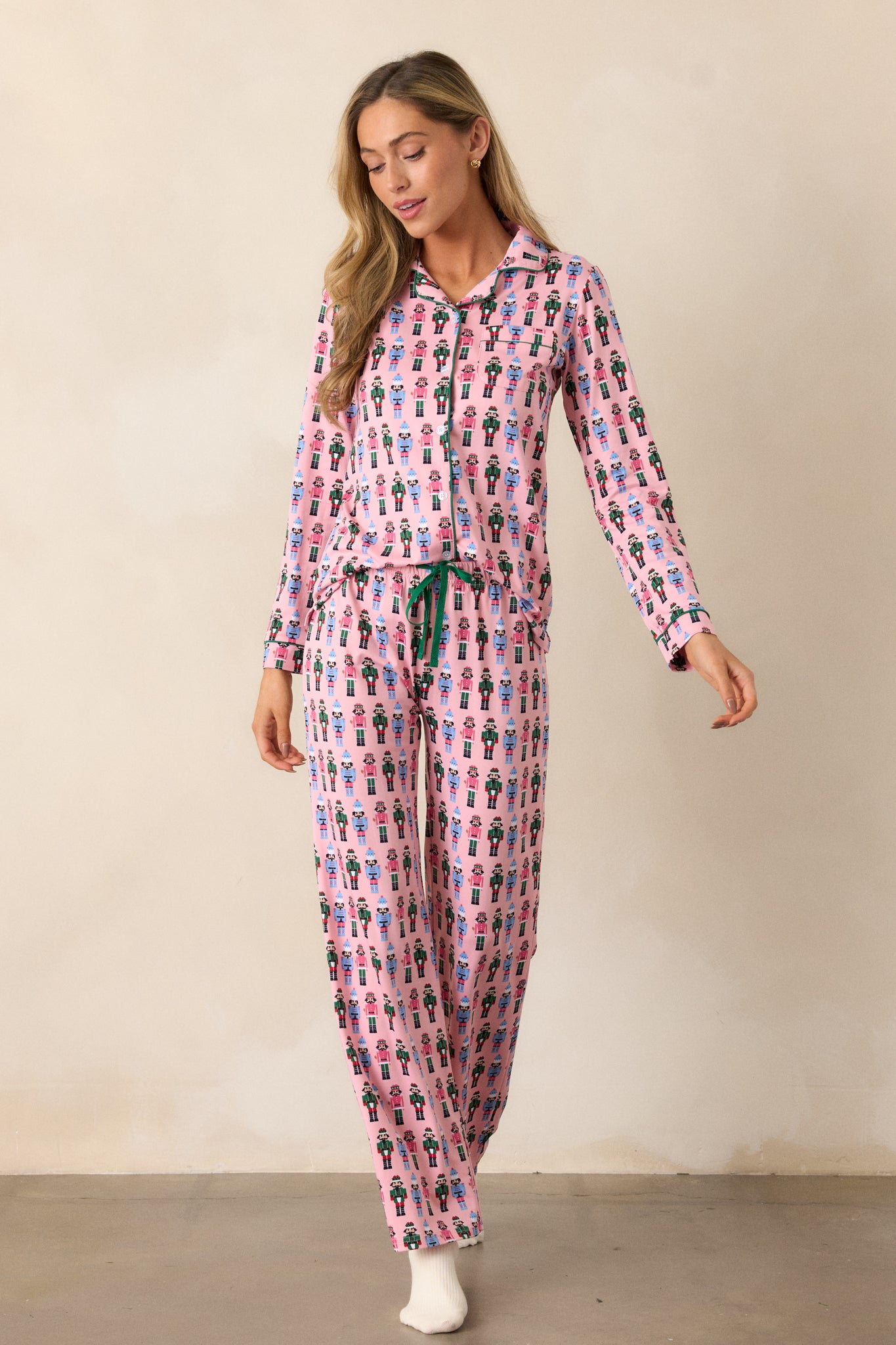 Pink pajama pants with a festive nutcracker pattern, showing a relaxed fit with a green tie on the elastic waistband.