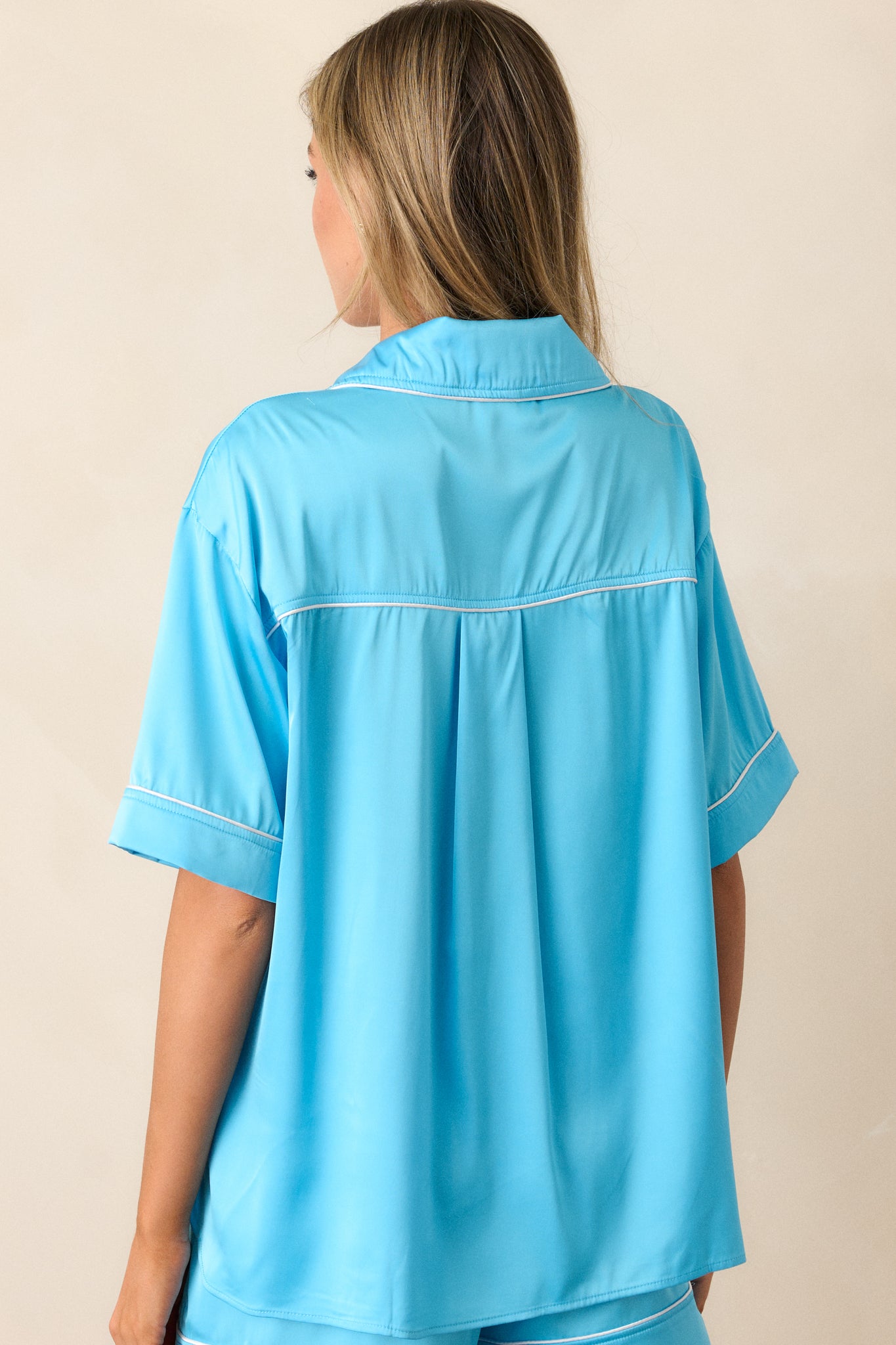 Back view of a blue pajama top highlighting the overall fit, white trim, and split hemline.