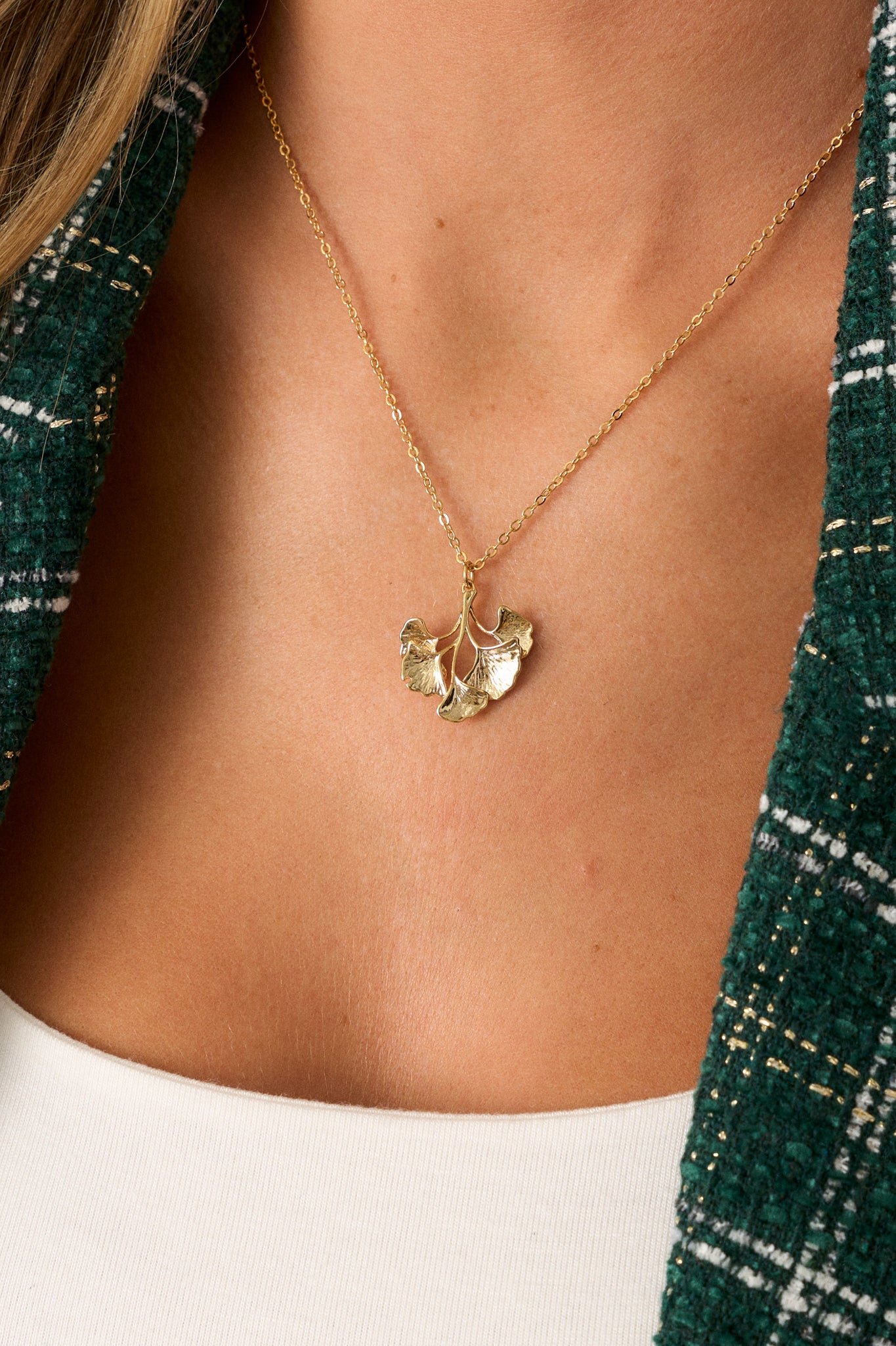 Close-up of the gold wildflower pendant on the necklace, focusing on the delicate design of the pendant and the smooth, thin gold chain.