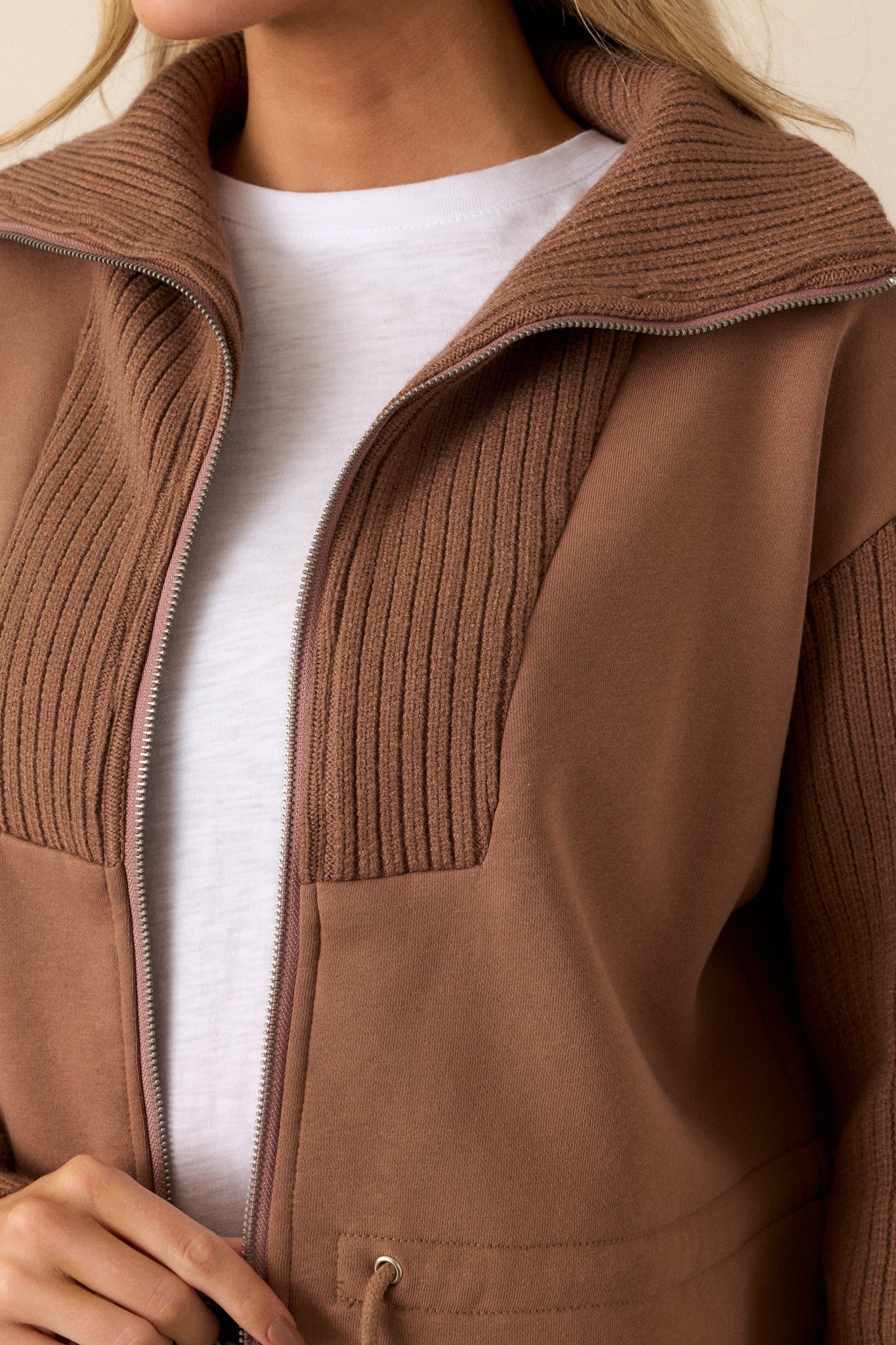 A close-up of the drawstring waistband on the brown jacket, showing the silver accents and the texture of the contrasting fabrics.