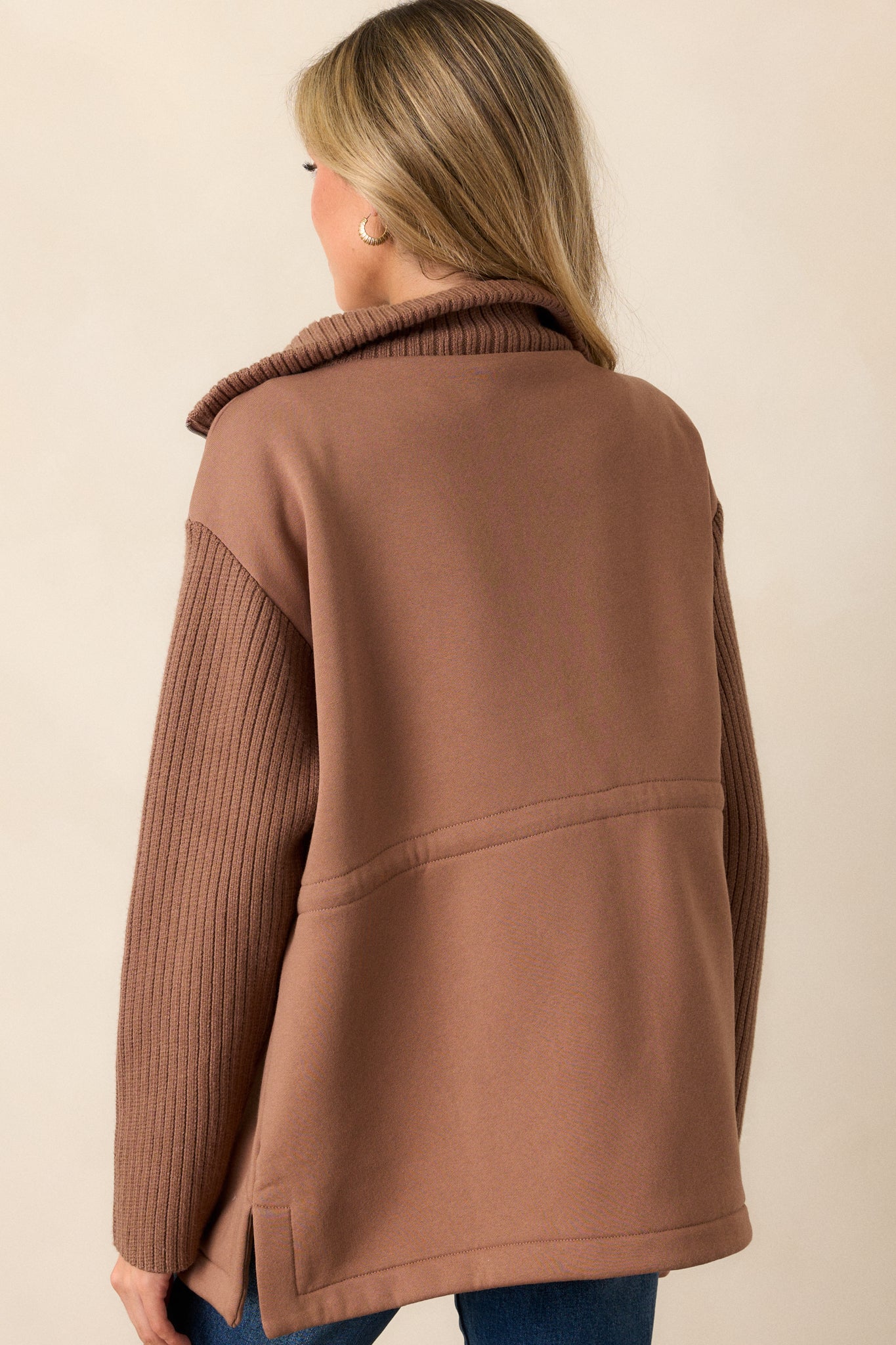 A back view of the brown jacket, featuring the long knit sleeves and the cinched waistband, showcasing the interplay of contrasting materials.