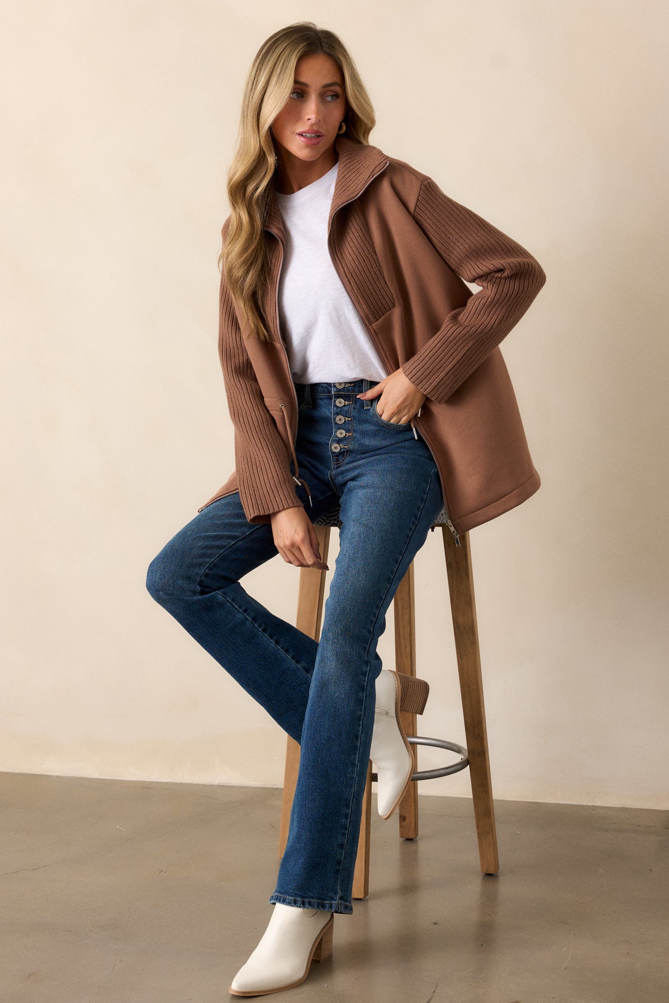 A front-facing view of the brown jacket, highlighting the contrasting fabrics, the drawstring cinch waistband with silver accents, and the long knit sleeves.