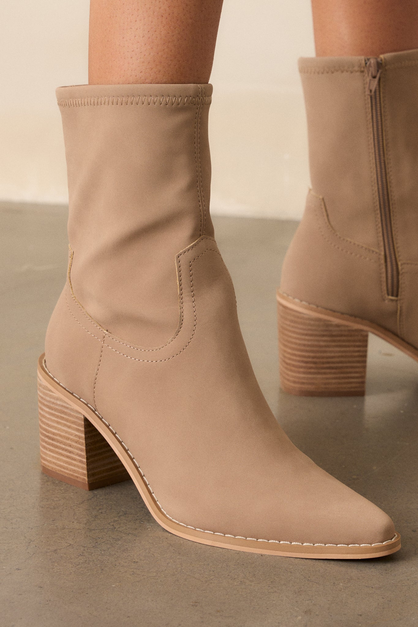 Close-up of these taupe boots that feature a pointed toe, a platform heel, a discrete side zipper and a tan sole.