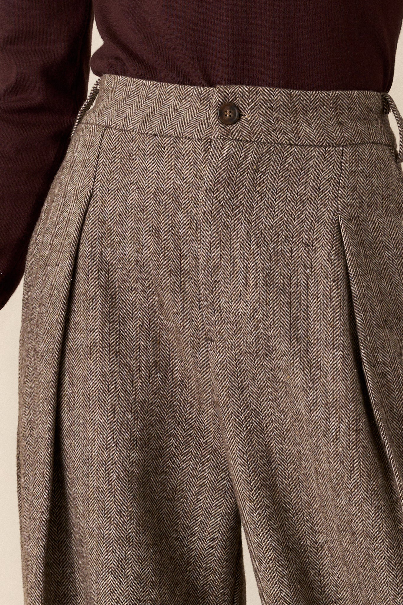 A detailed close-up of the brown pants, highlighting the herringbone design in the fabric and the stitching around the functional back pockets. The texture and craftsmanship are the focal points.