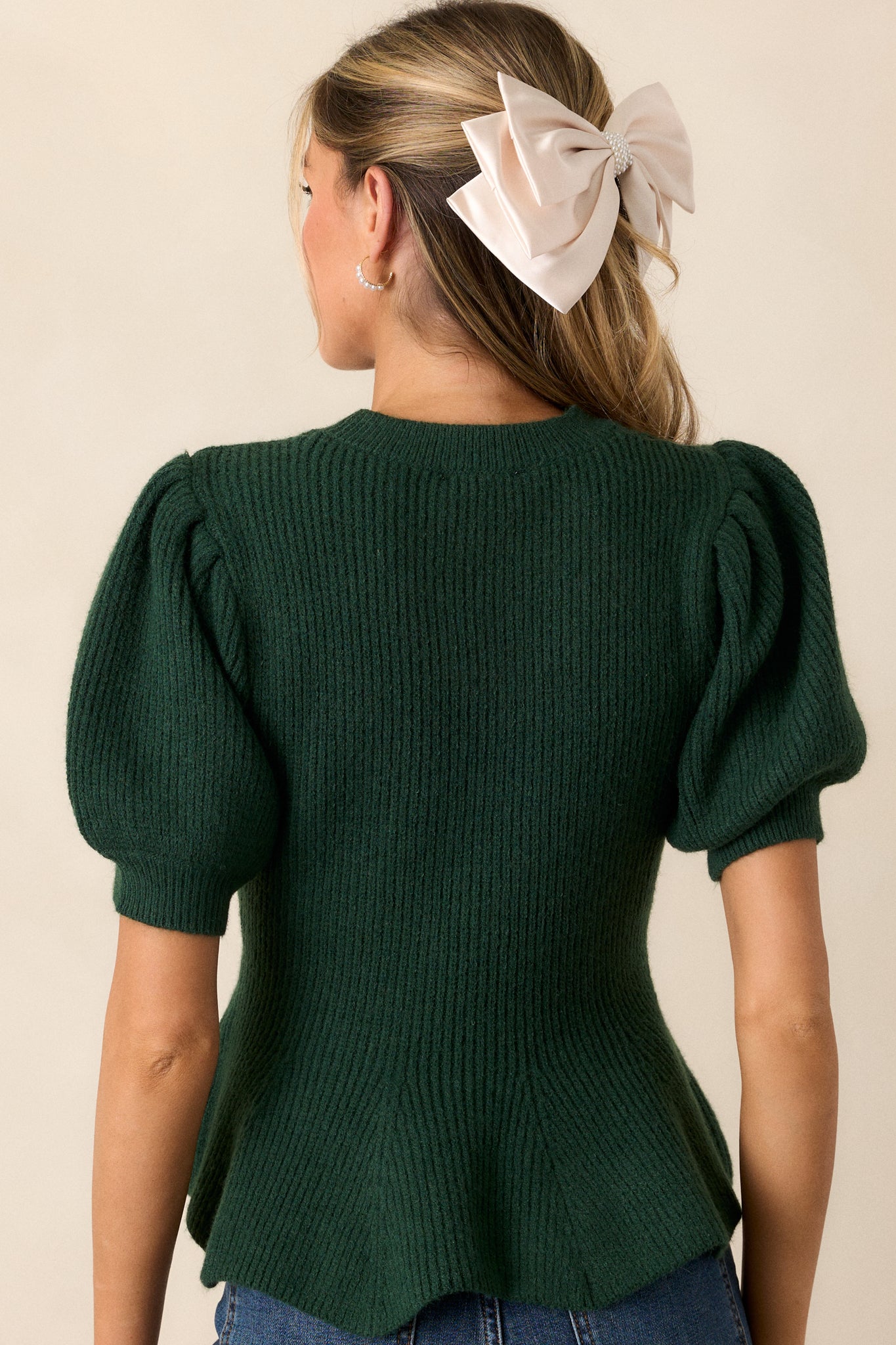 A back view of the green sweater, highlighting the peplum silhouette and puff sleeves with ribbed cuffs.