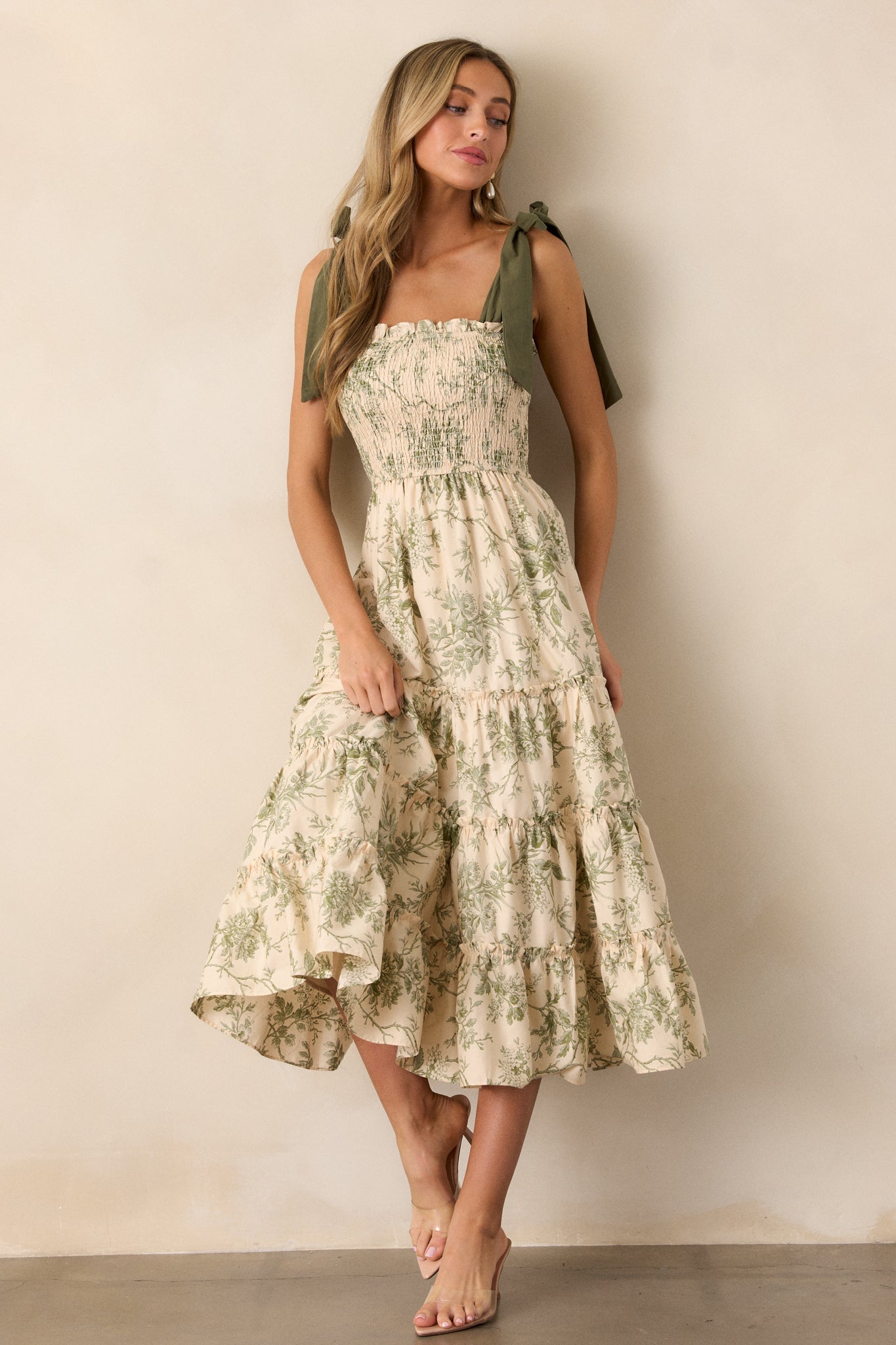 An ivory midi dress with a green floral pattern, featuring a smocked bodice and green ribbon shoulder straps, seen from the front.