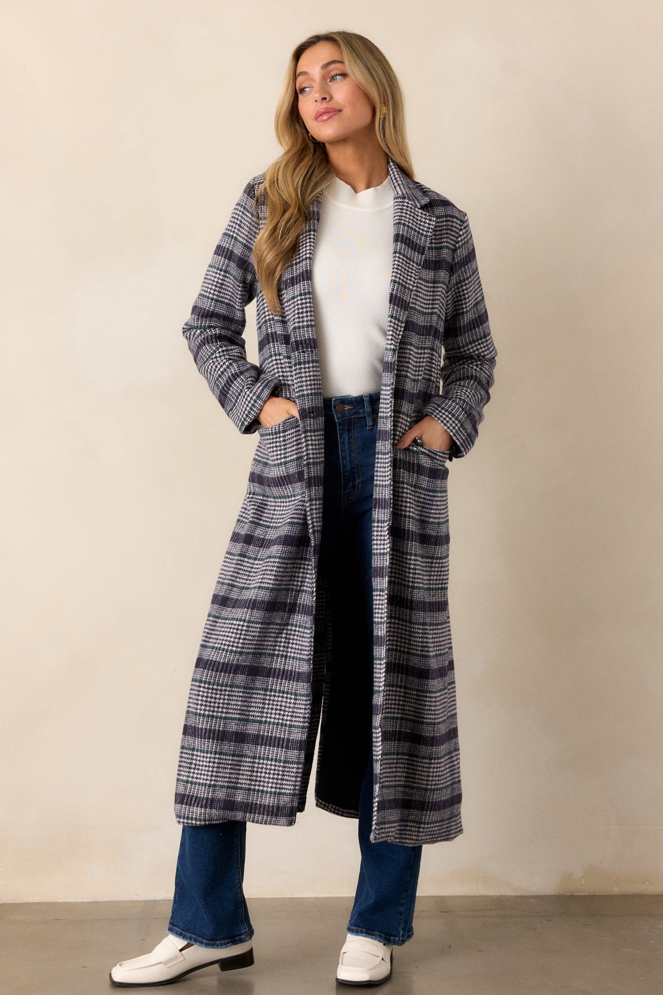 A navy plaid coat featuring a lapel collar, functional button front, midi-length cut, functional pockets, and long sleeves with button detailing.